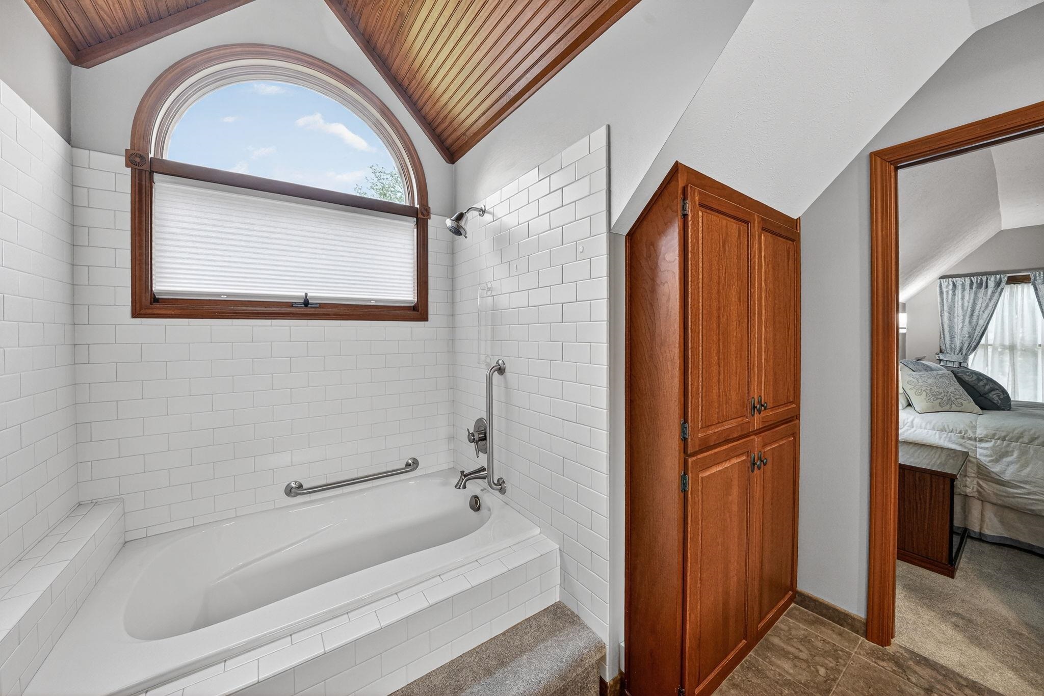 Alcove bathtub featuring subway tile surround, wood-finish arch window, and wood-paneled ceiling