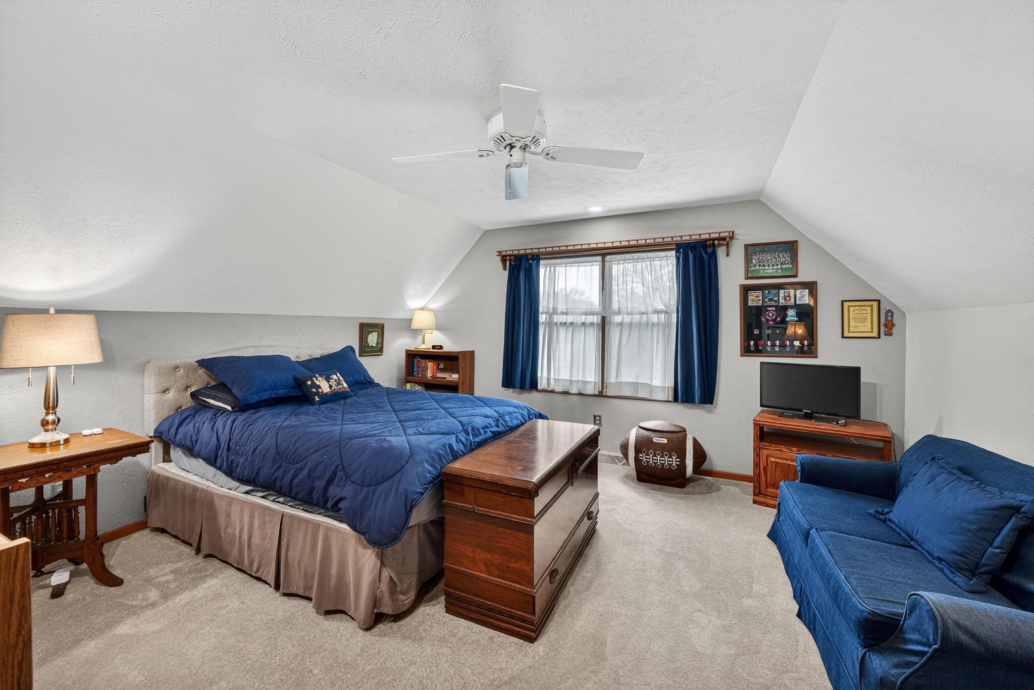 Sloped ceilings define this room, featuring carpeting and a central ceiling fan
