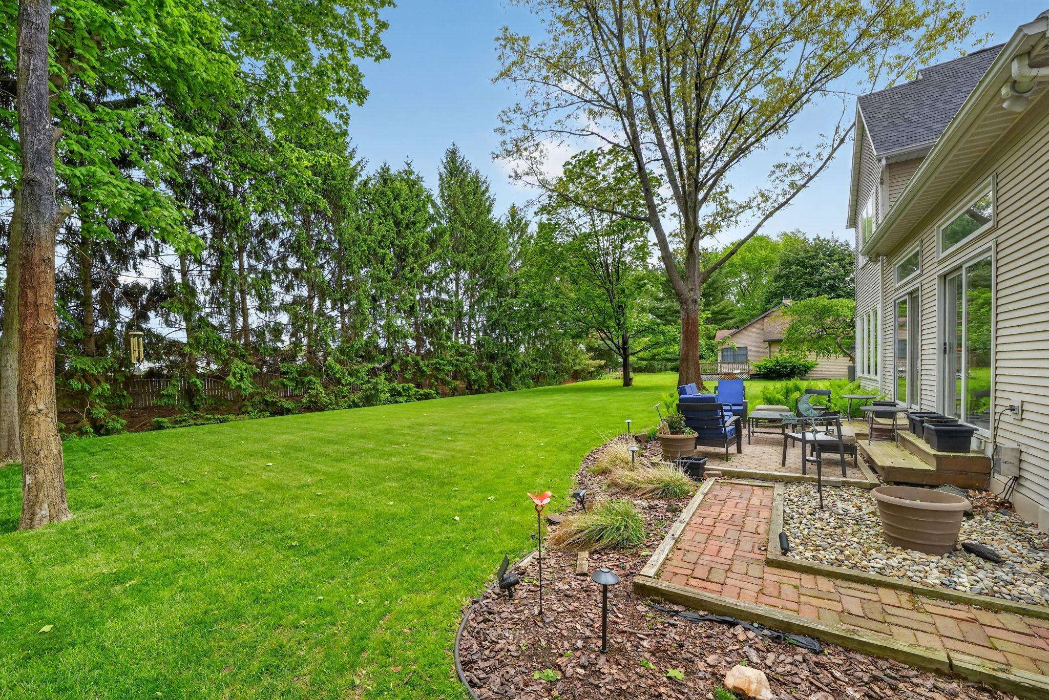 Expansive backyard featuring a large lawn, mature trees, and a brick paver patio