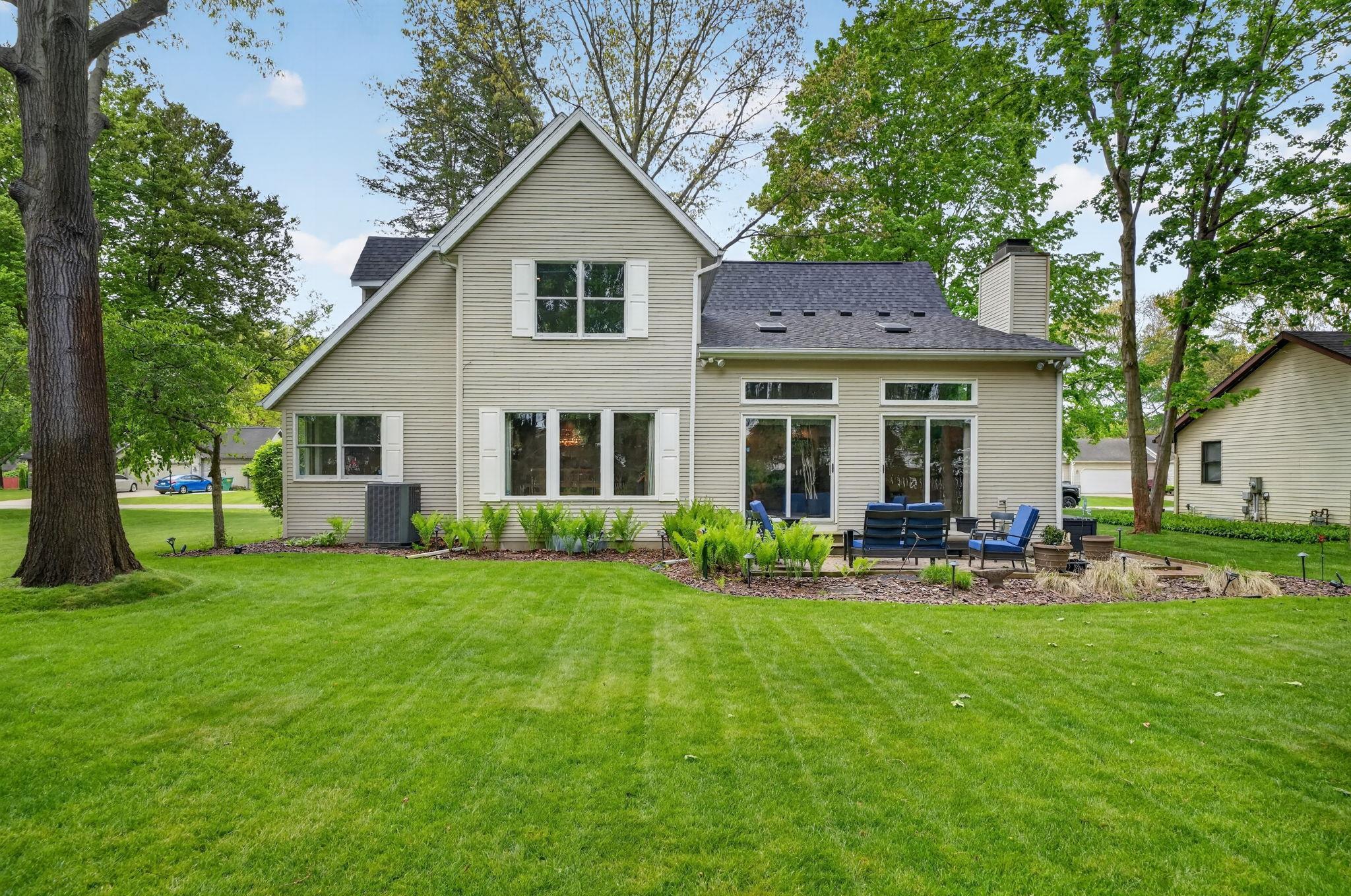 Expansive green lawn with a residential structure featuring light-colored siding, white window shutters, and a dark shingle roof
