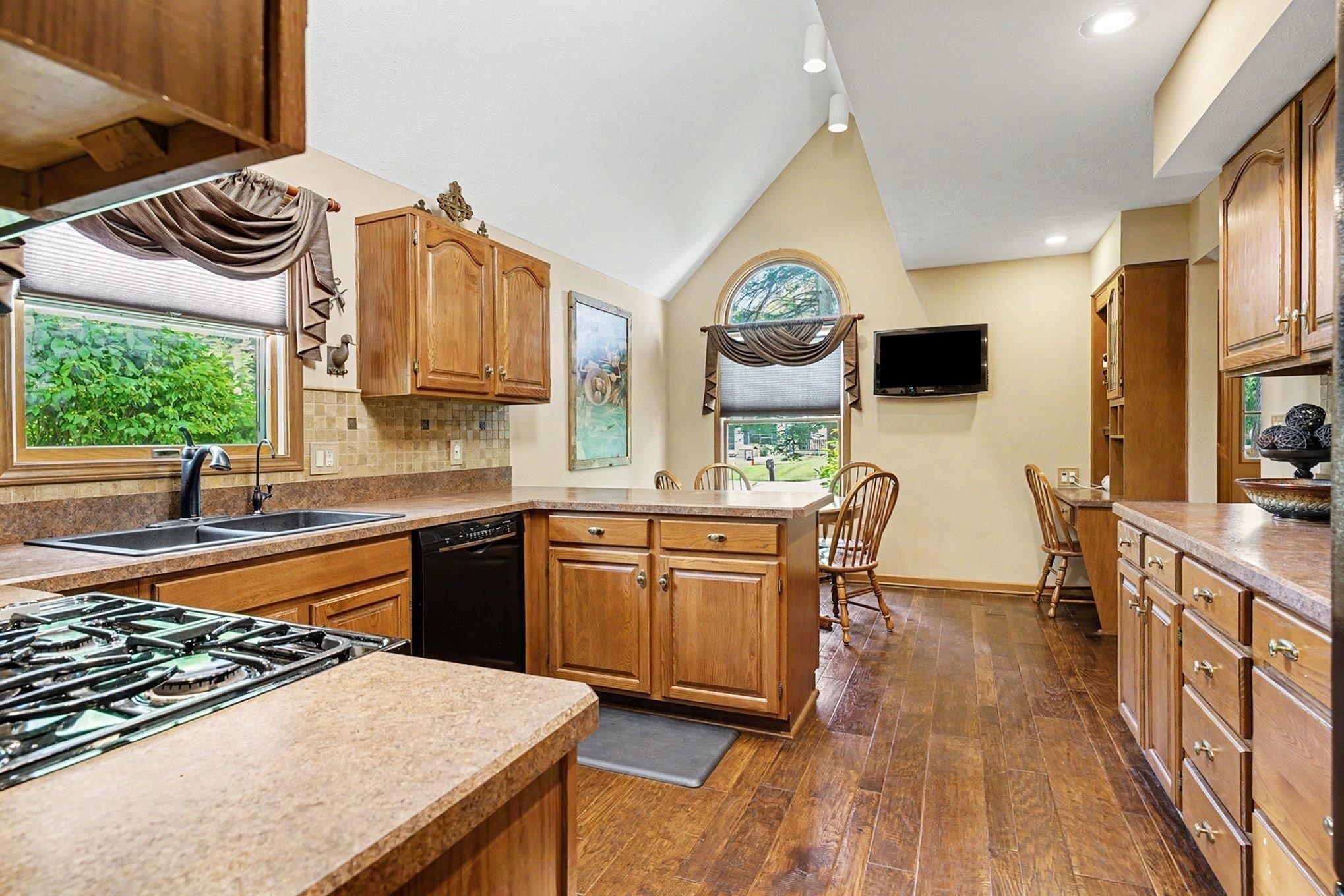 Kitchen featuring wood-finish flooring, warm-toned cabinetry, light-colored countertops, and a tile backsplash