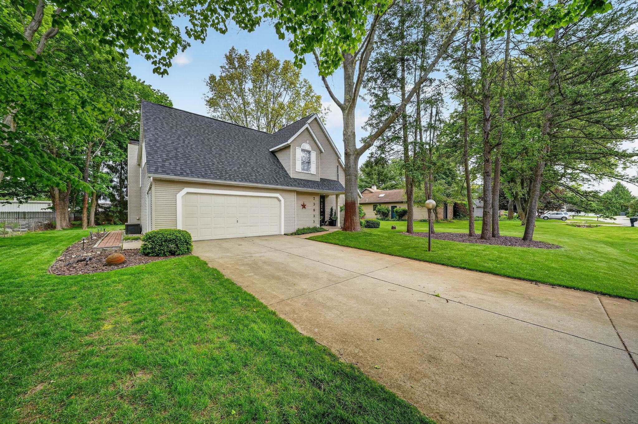 Two-story residence featuring a neutral exterior, attached garage, concrete driveway, and mature landscaping