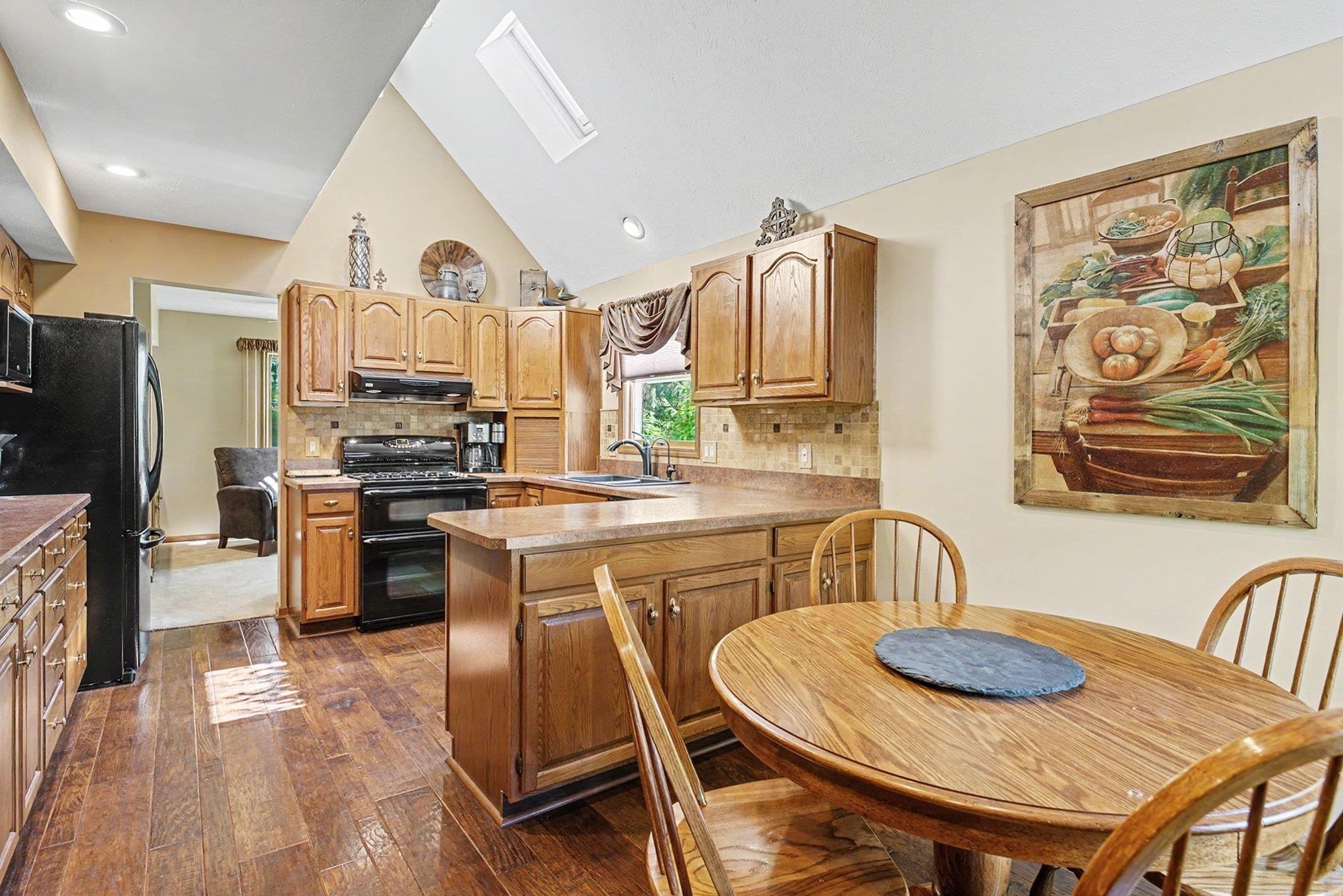 Kitchen featuring vaulted ceilings, skylight, recessed lighting, wood-finish flooring, and wood cabinetry