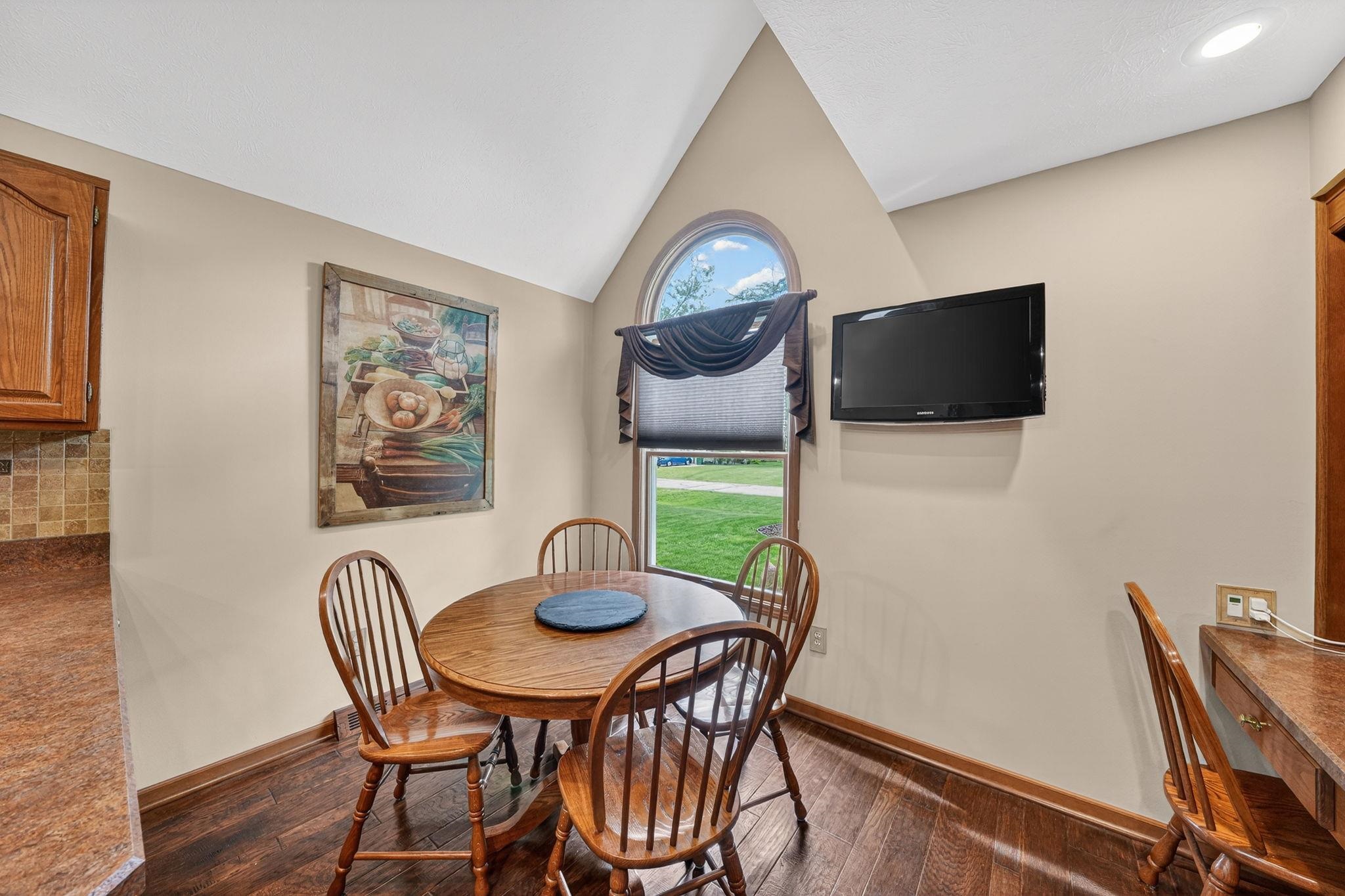 Breakfast nook featuring a vaulted ceiling with recessed lighting, a built-in wood-finish desk, and a large arched window