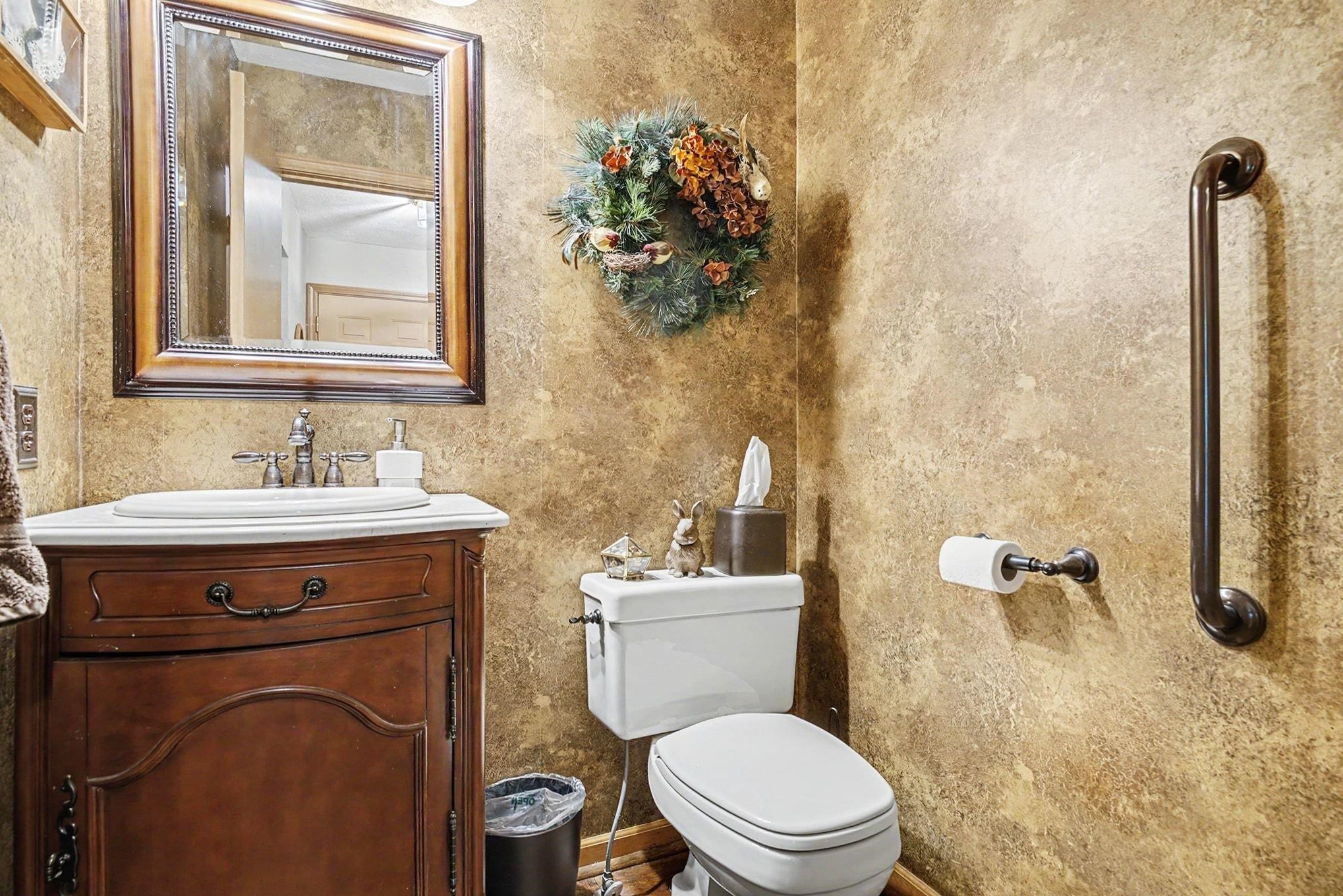 Bathroom featuring a wood vanity with a drop-in sink, framed wall mirror, toilet with standard flush, and an oil-rubbed bronze grab bar