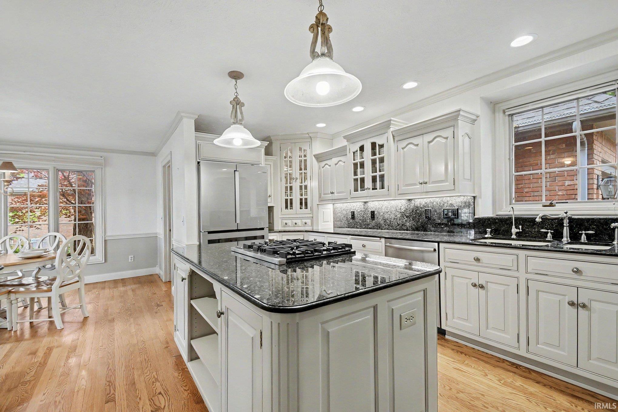 Kitchen featuring hardwood flooring, white cabinetry, a large center island with a built-in cooktop, dark speckled countertops, and stainless steel appliances