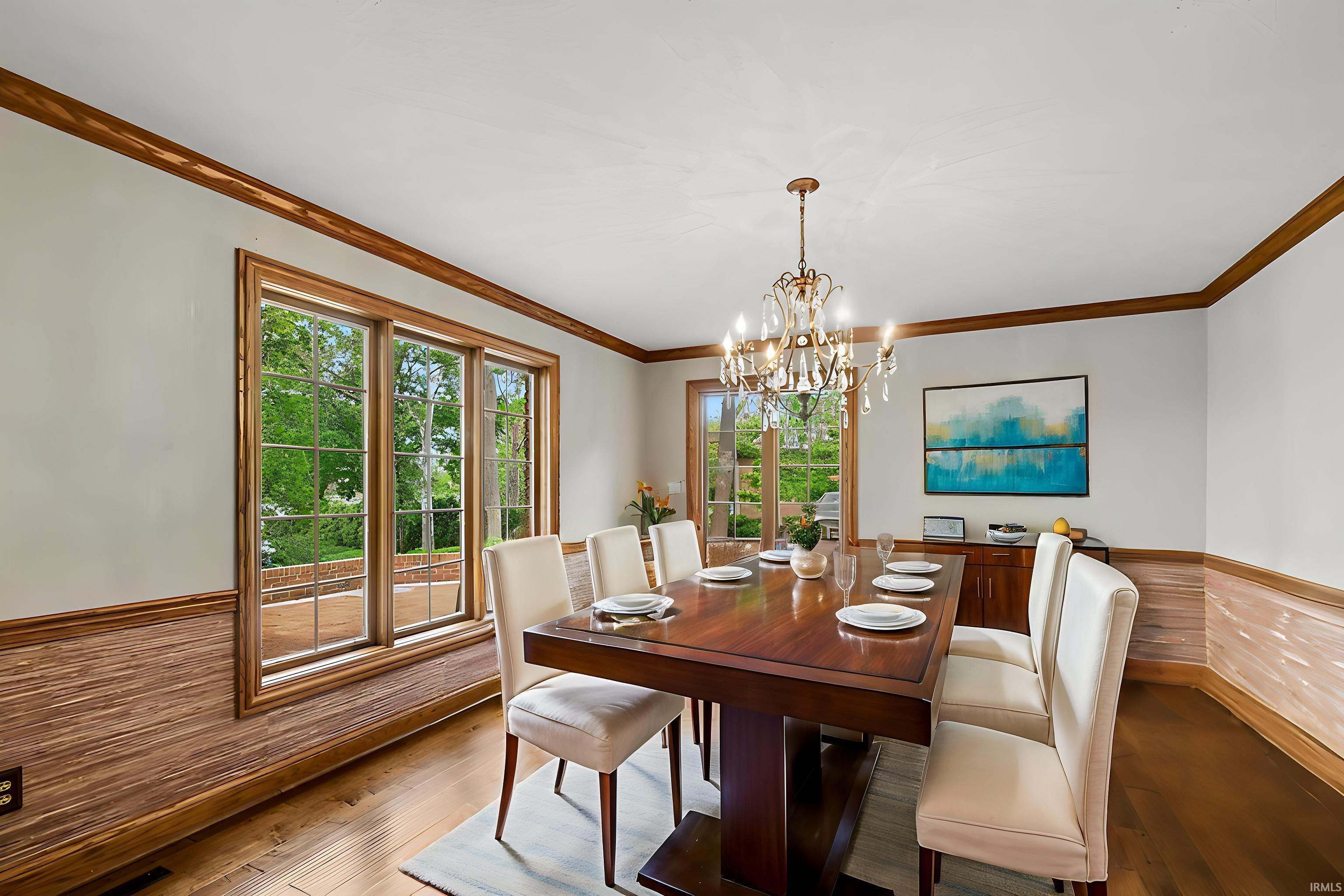 Dining space featuring wood-finish flooring, a crystal chandelier, wood window trim, a large picture window, and wainscoting