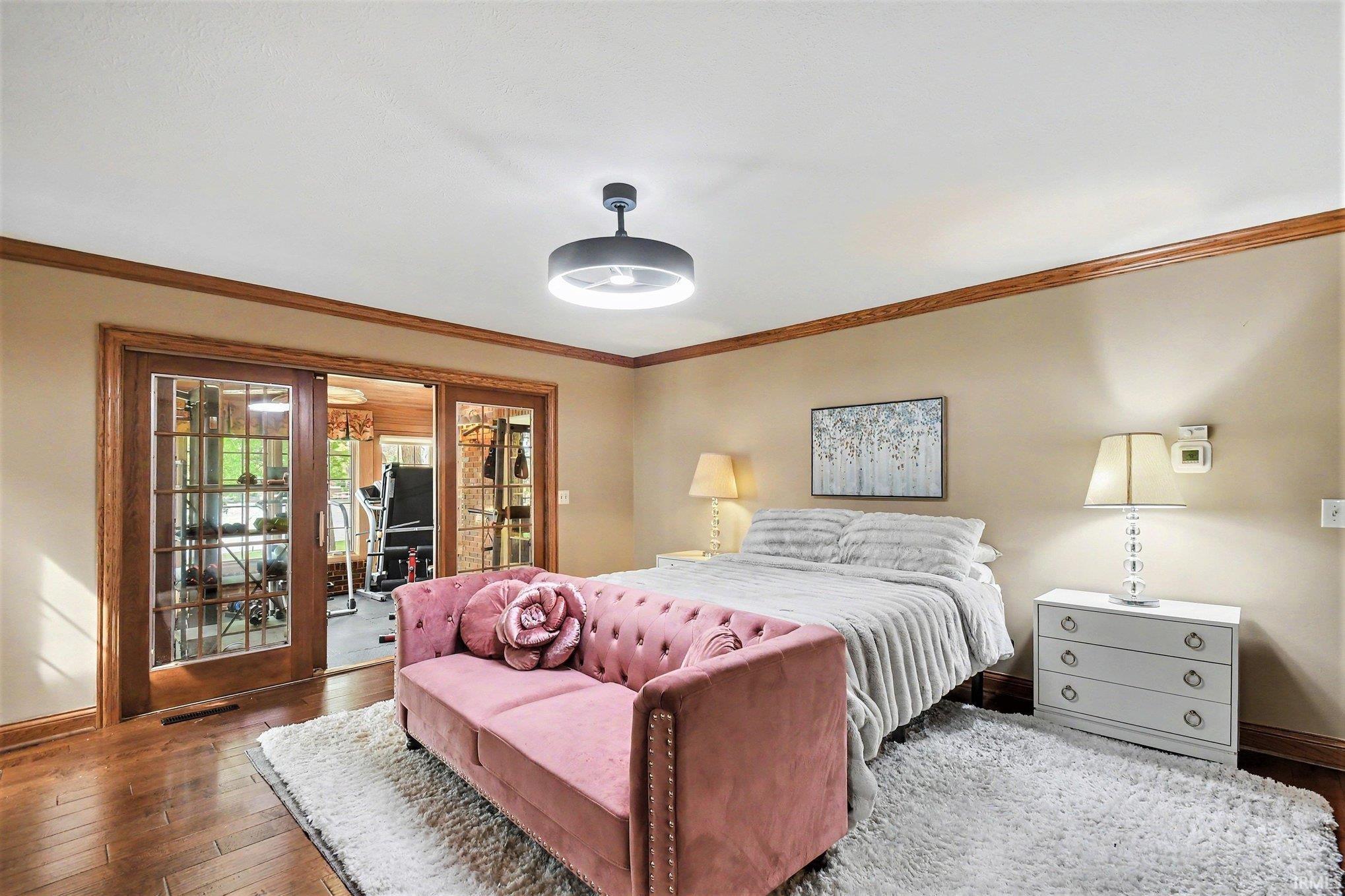Room featuring hardwood flooring, crown molding, and a modern ceiling fixture.