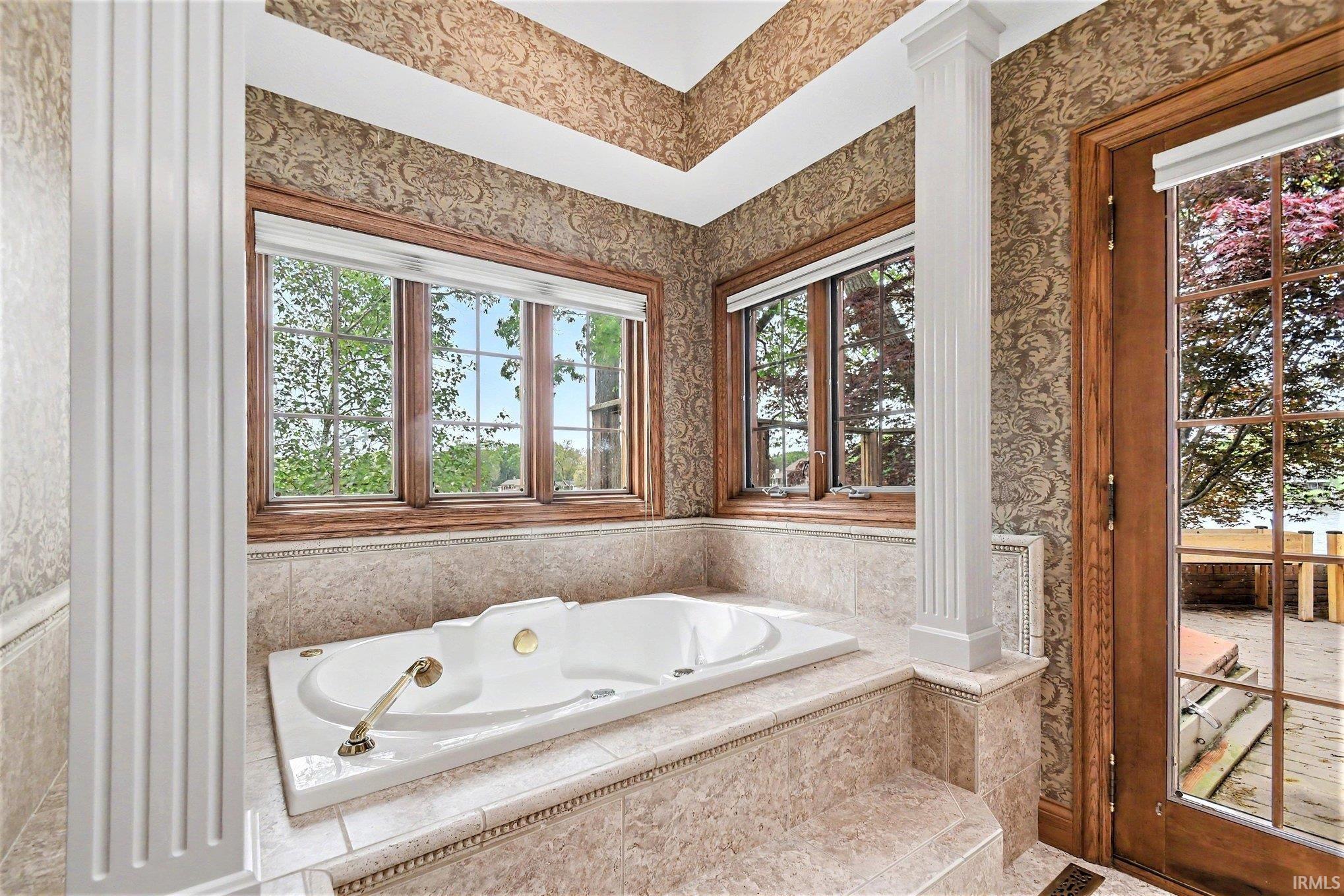 Built-in soaking tub with brass fixtures, surrounded by tile decking and framed by two multi-pane windows