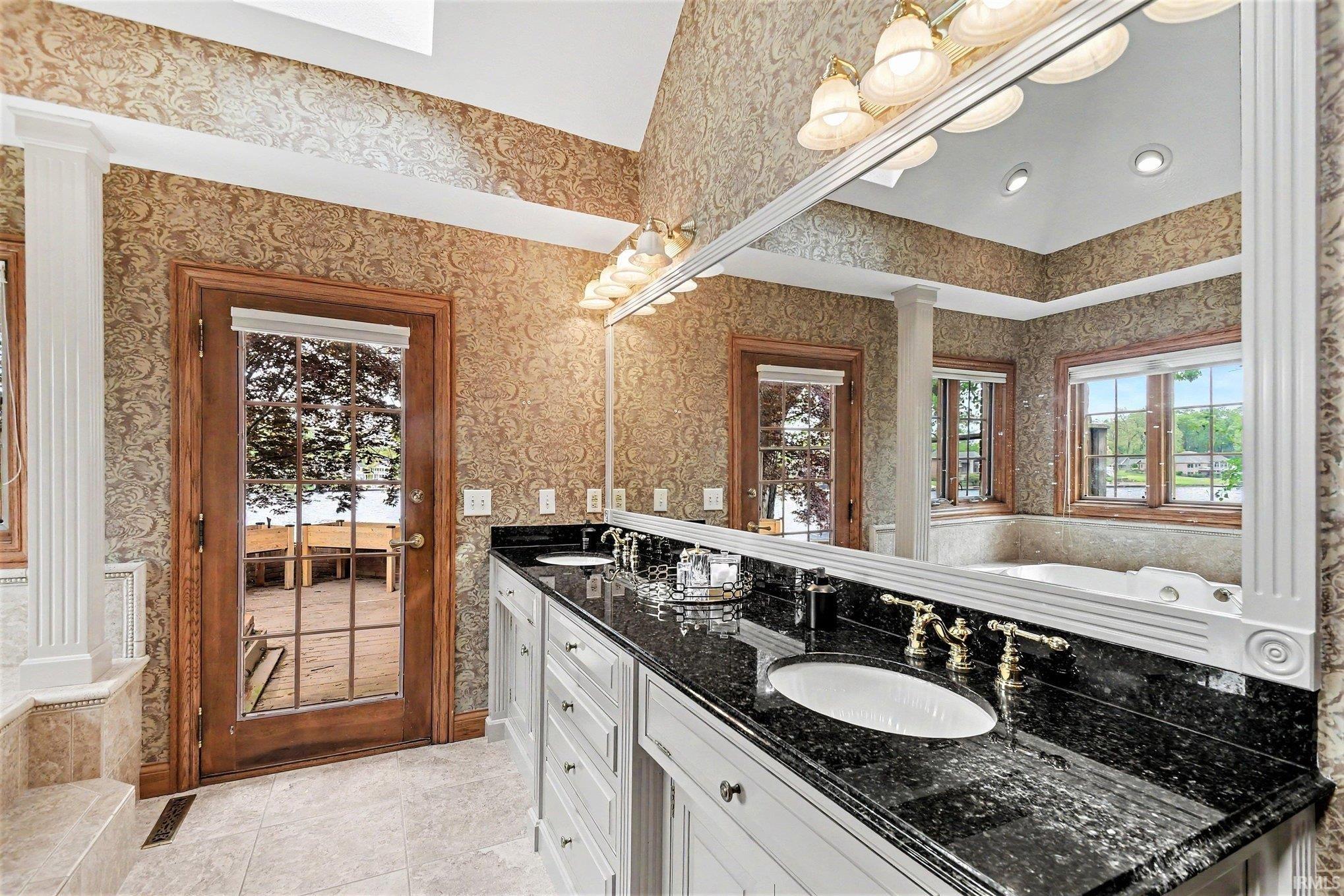 Dual vanity featuring integrated sinks, dark stone countertop, and brass-finish fixtures