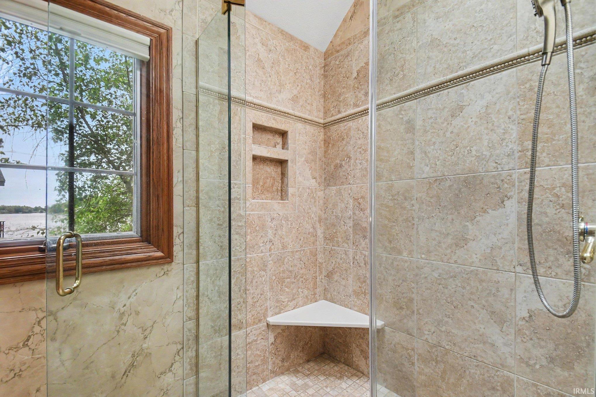 Tiled shower enclosure featuring a corner bench, recessed shelving, and a handheld showerhead
