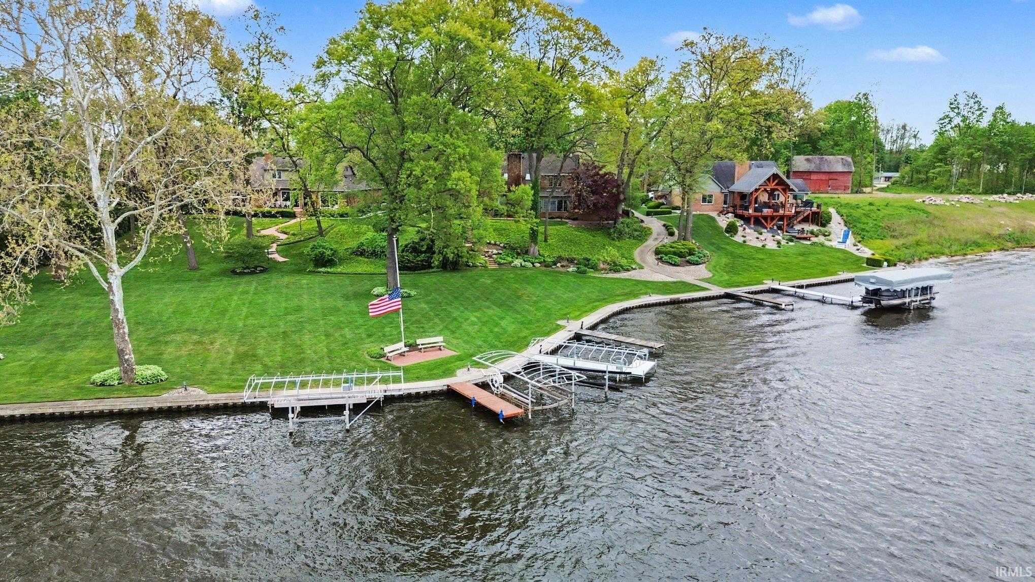 Waterfront property featuring extensive green lawn, mature trees, multiple docks, and a boat lift