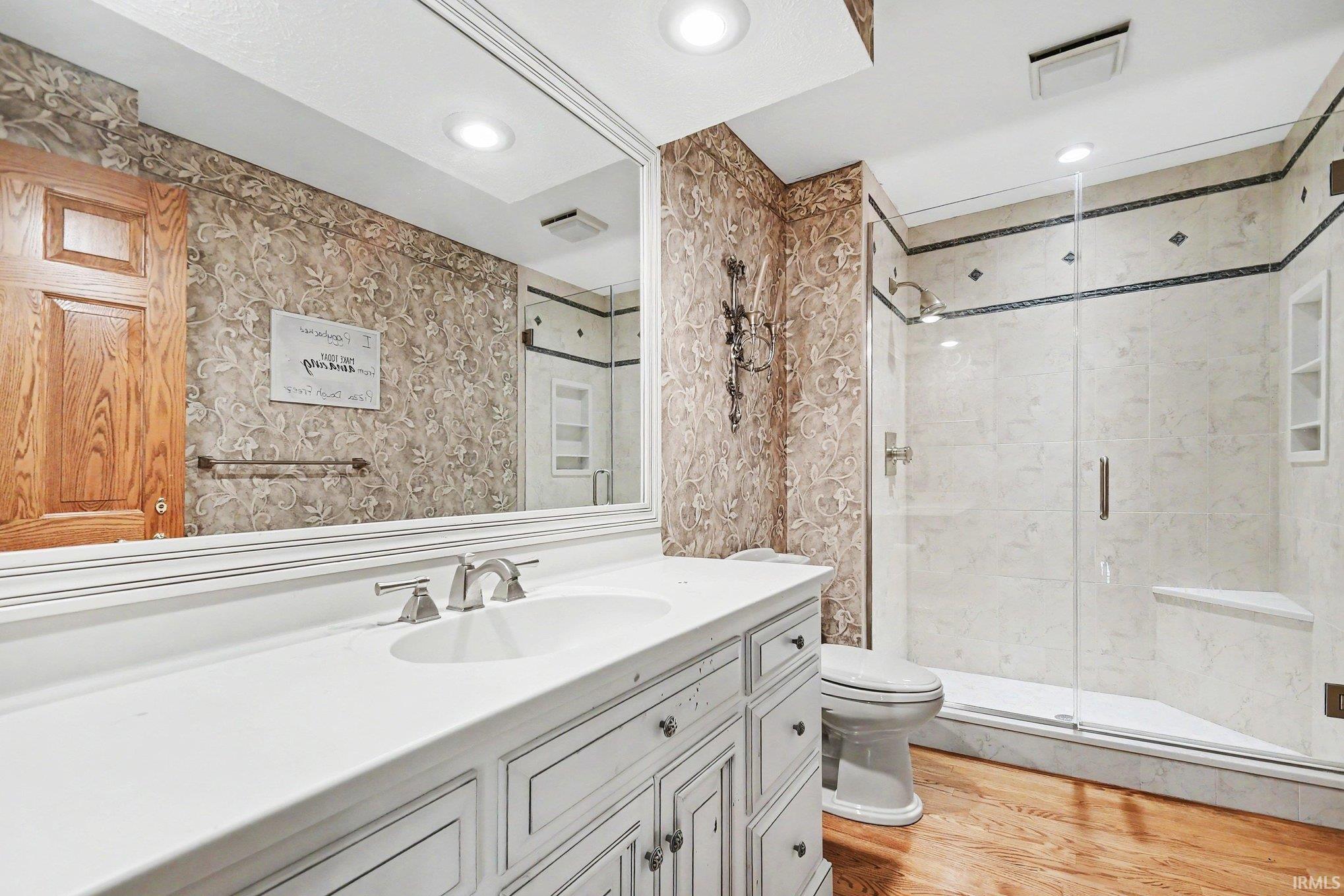 Bathroom featuring a white vanity with integrated sink, a large wall-mounted mirror, and wood-finish flooring