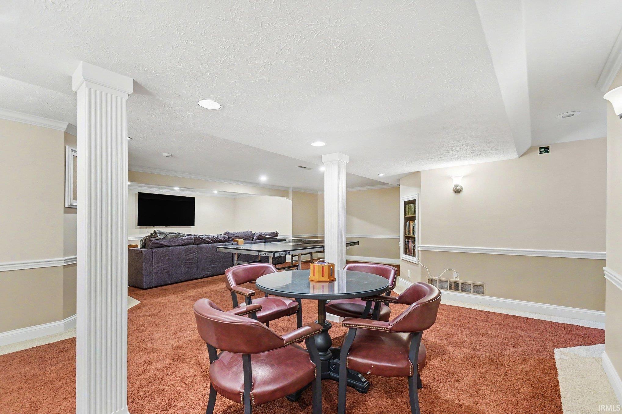 Spacious finished lower level featuring recessed lighting, a built-in bookshelf, wall sconces, and architectural columns