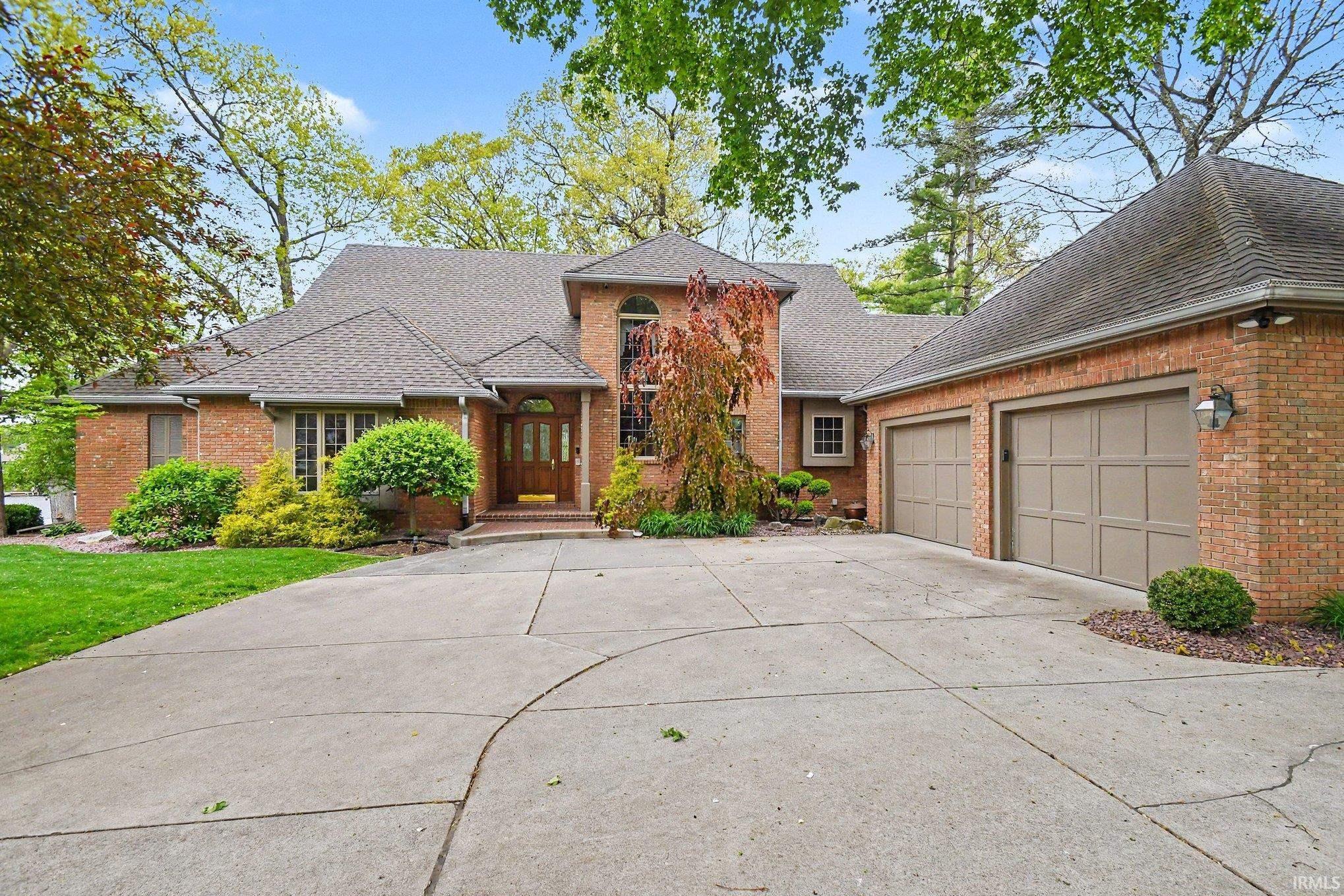 Brick exterior featuring a multi-paneled front door with sidelights, a circular driveway, and an attached two-car garage with panel-style doors