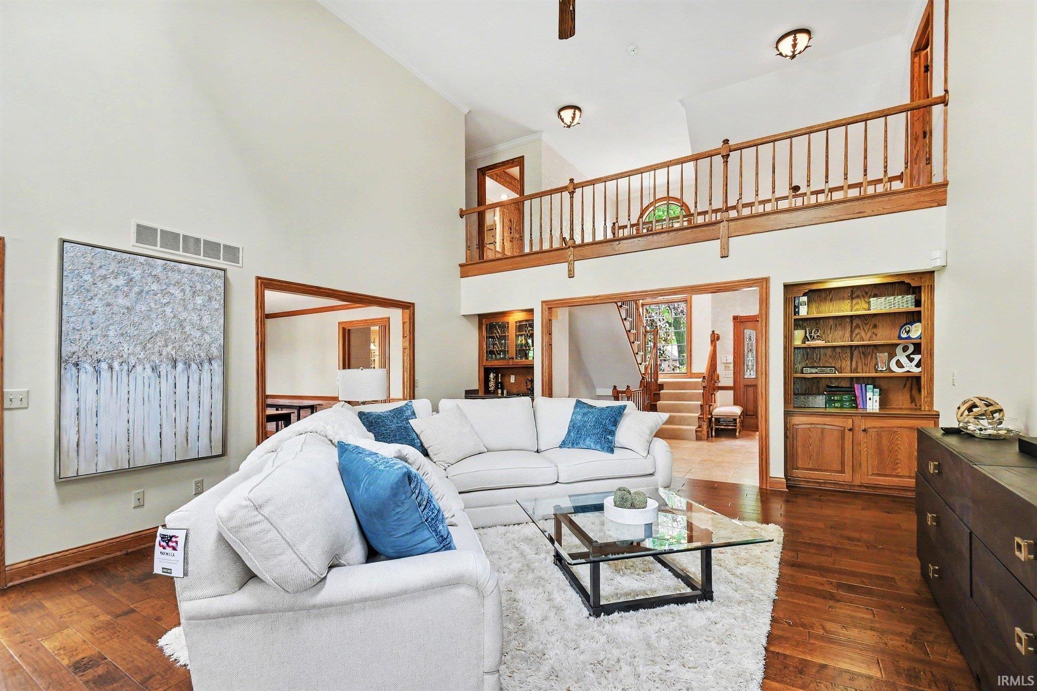 Great room featuring vaulted ceilings, wood-finish flooring, a second-story balcony with wood railing, and a built-in wood bookcase
