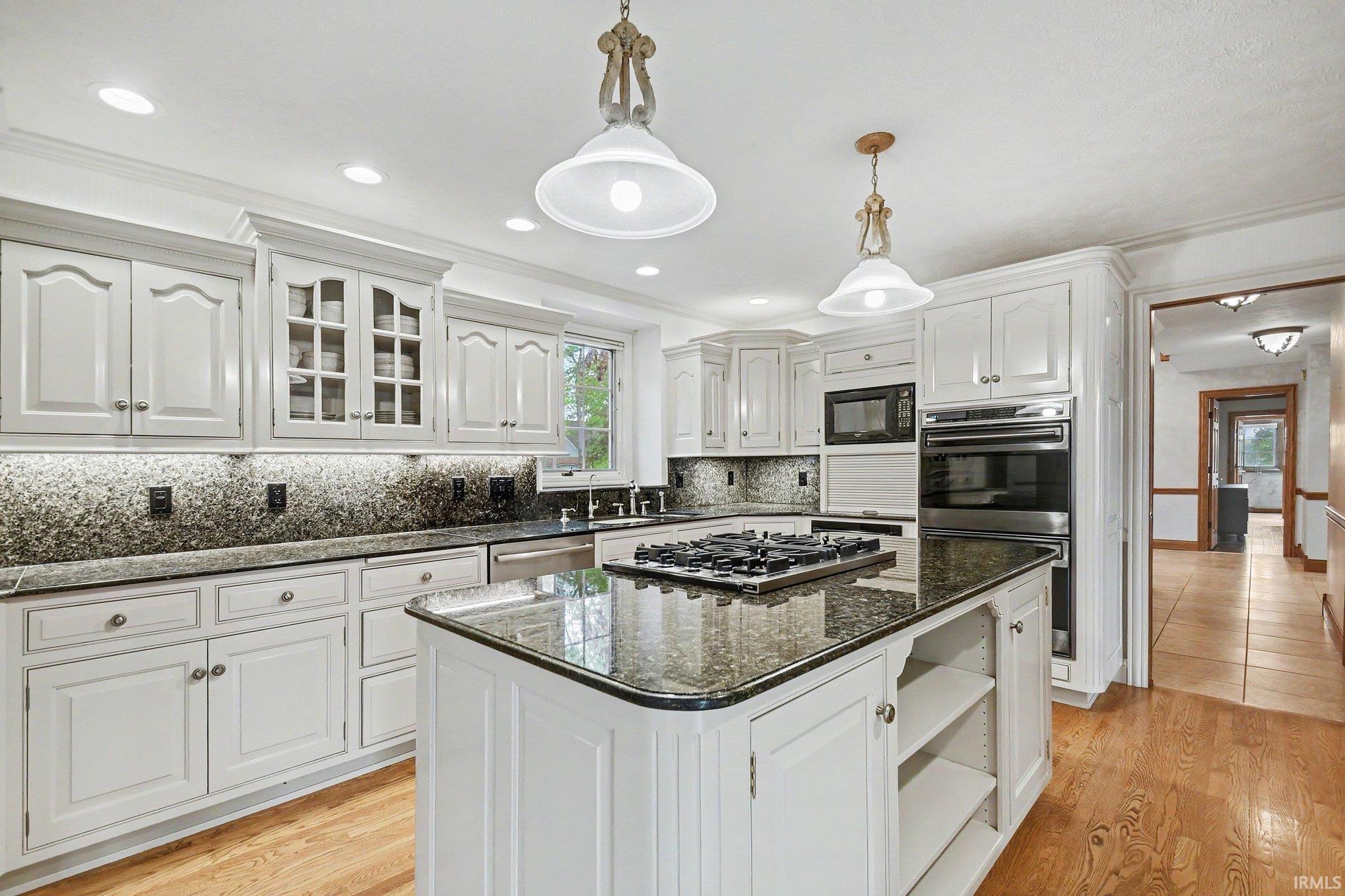 Kitchen featuring white cabinetry with glass-front accents, dark granite countertops, and a large center island with a built-in cooktop