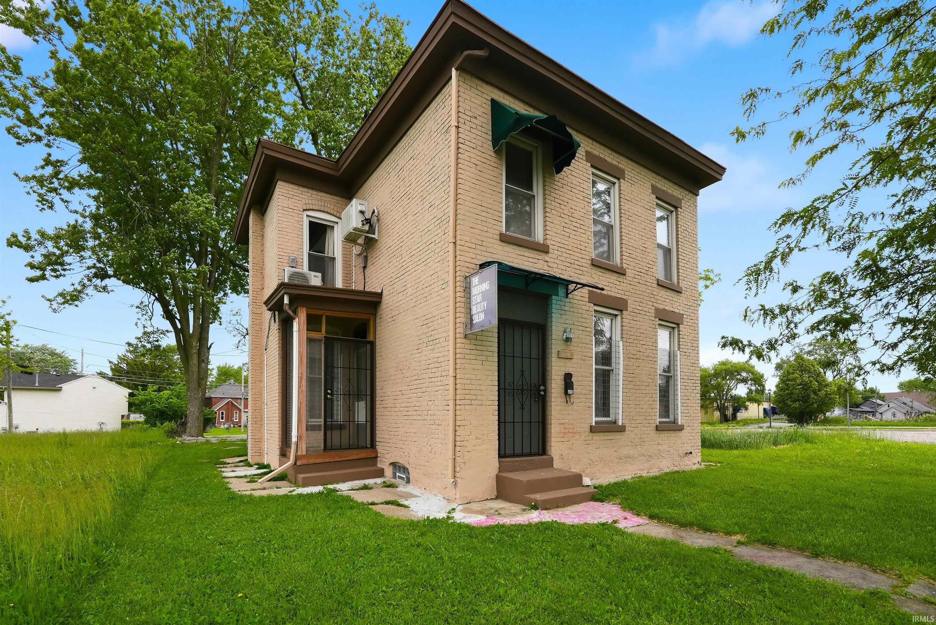 Two-story brick exterior featuring multiple windows with awnings, a front entry with security door, and a side entry with a screen door
