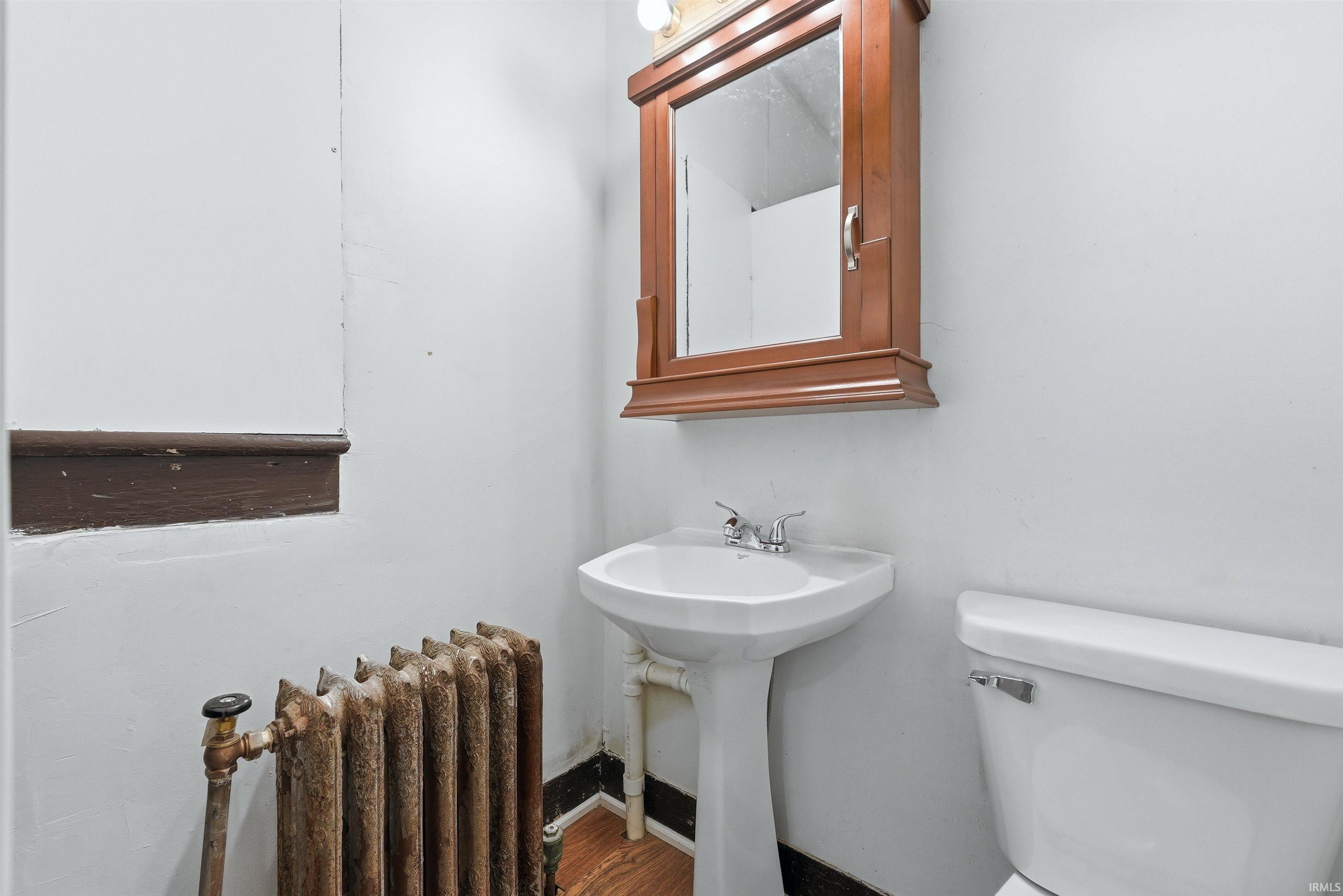 Pedestal sink with chrome faucet, complemented by a wall-mounted wooden medicine cabinet featuring a mirror