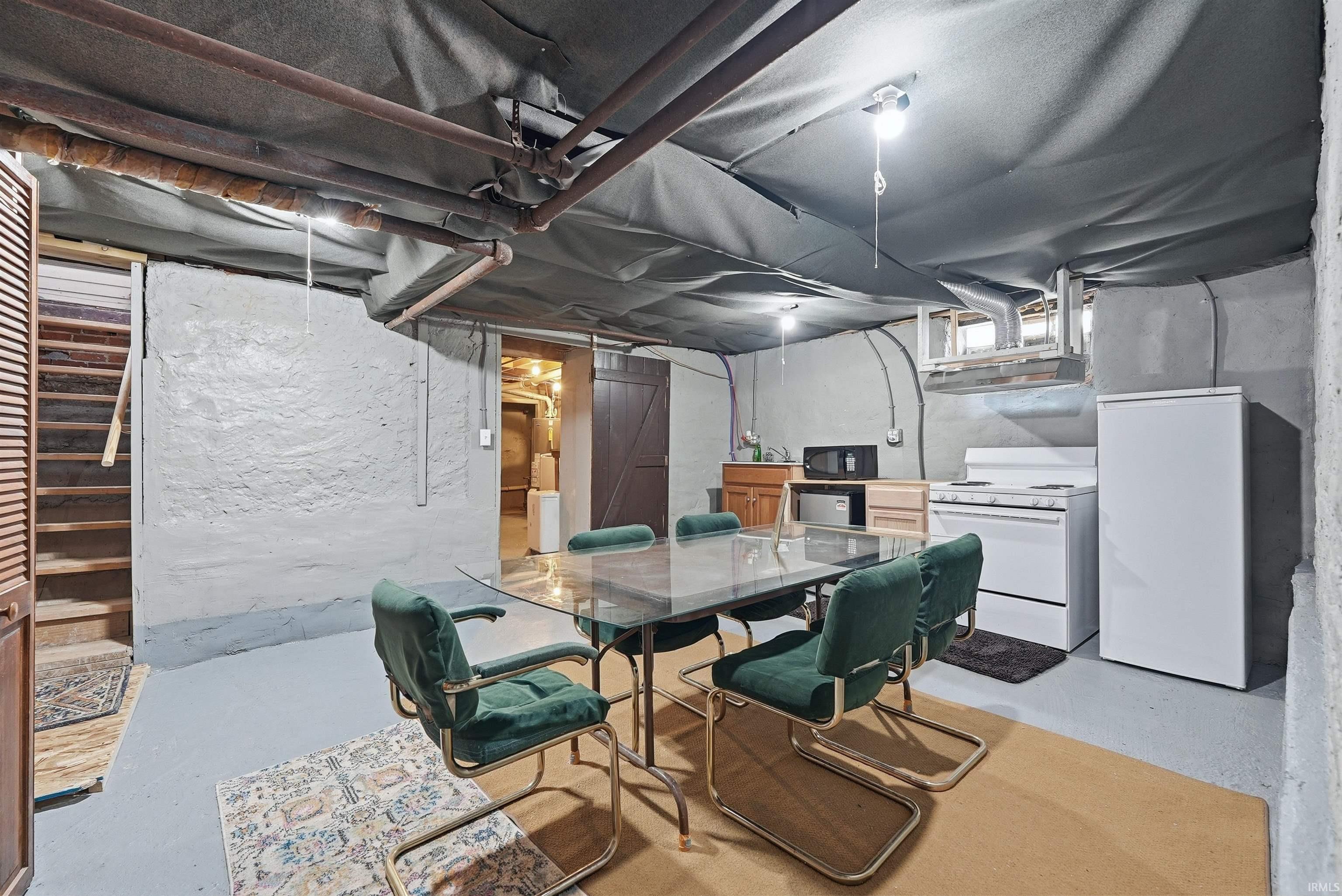 Finished lower level featuring painted concrete walls, exposed ceiling joists with insulation, a glass-top dining table, a built-in countertop with an integrated sink, and an exposed wood staircase