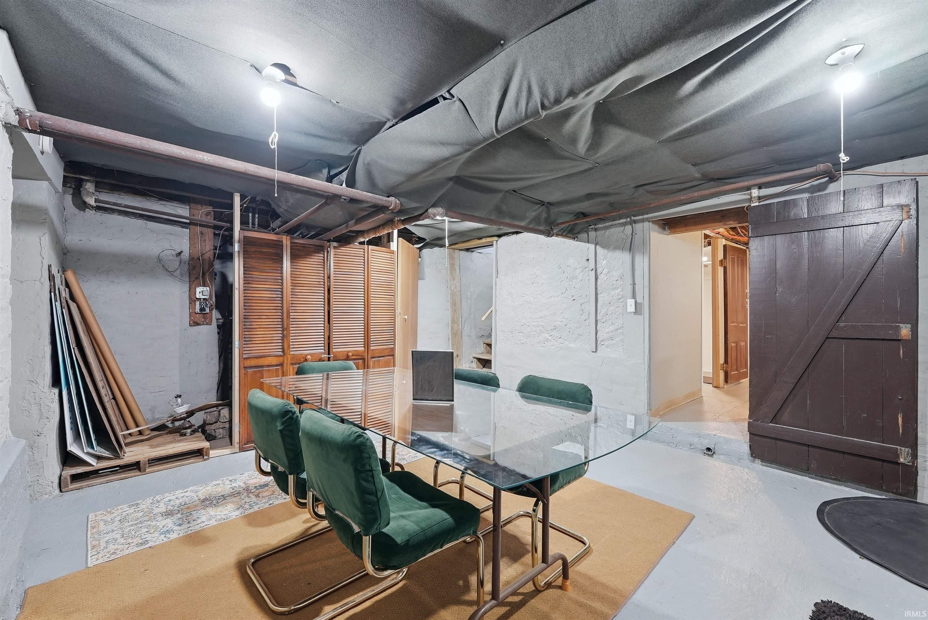 Finished lower level space featuring a wide-plank wood door, louvered wood folding doors, painted concrete flooring, exposed overhead piping, and overhead bare bulb lighting