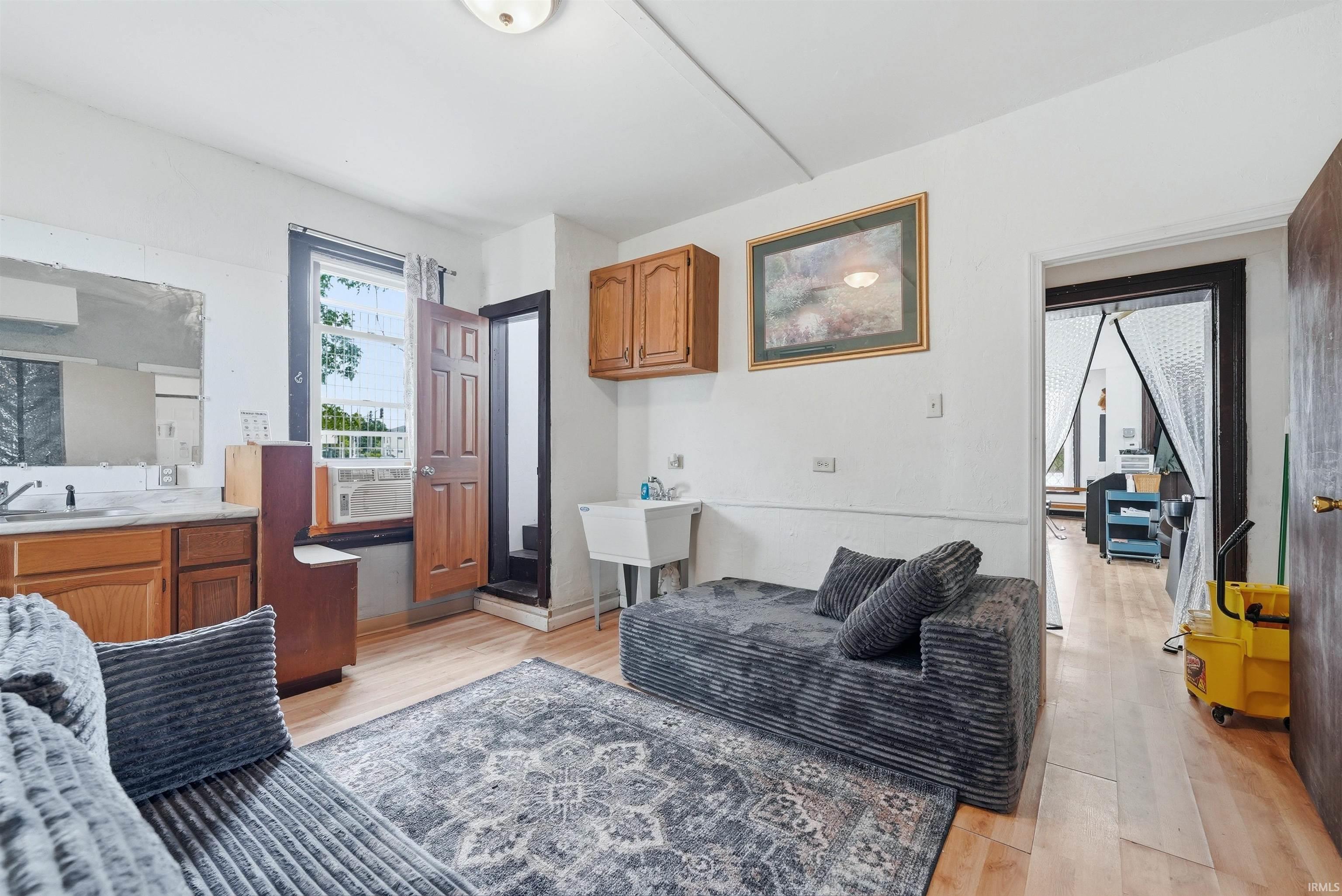 Back room living space. Light wood-finish flooring throughout, featuring a functional sink area with wood cabinetry and countertop