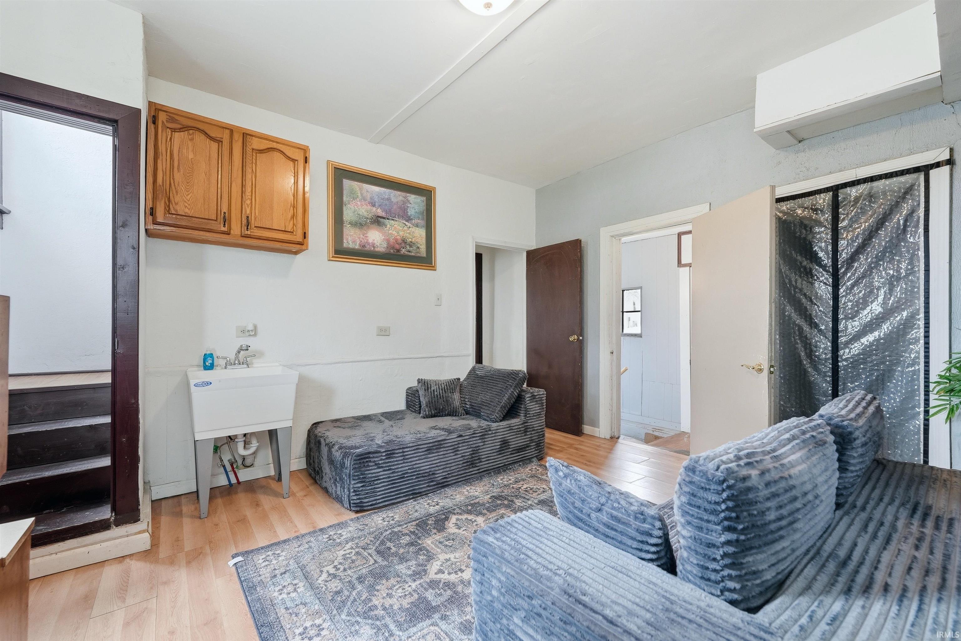 Back room living space. Utility area featuring a wall-mounted laundry sink, overhead wood cabinetry, and wood-finish flooring