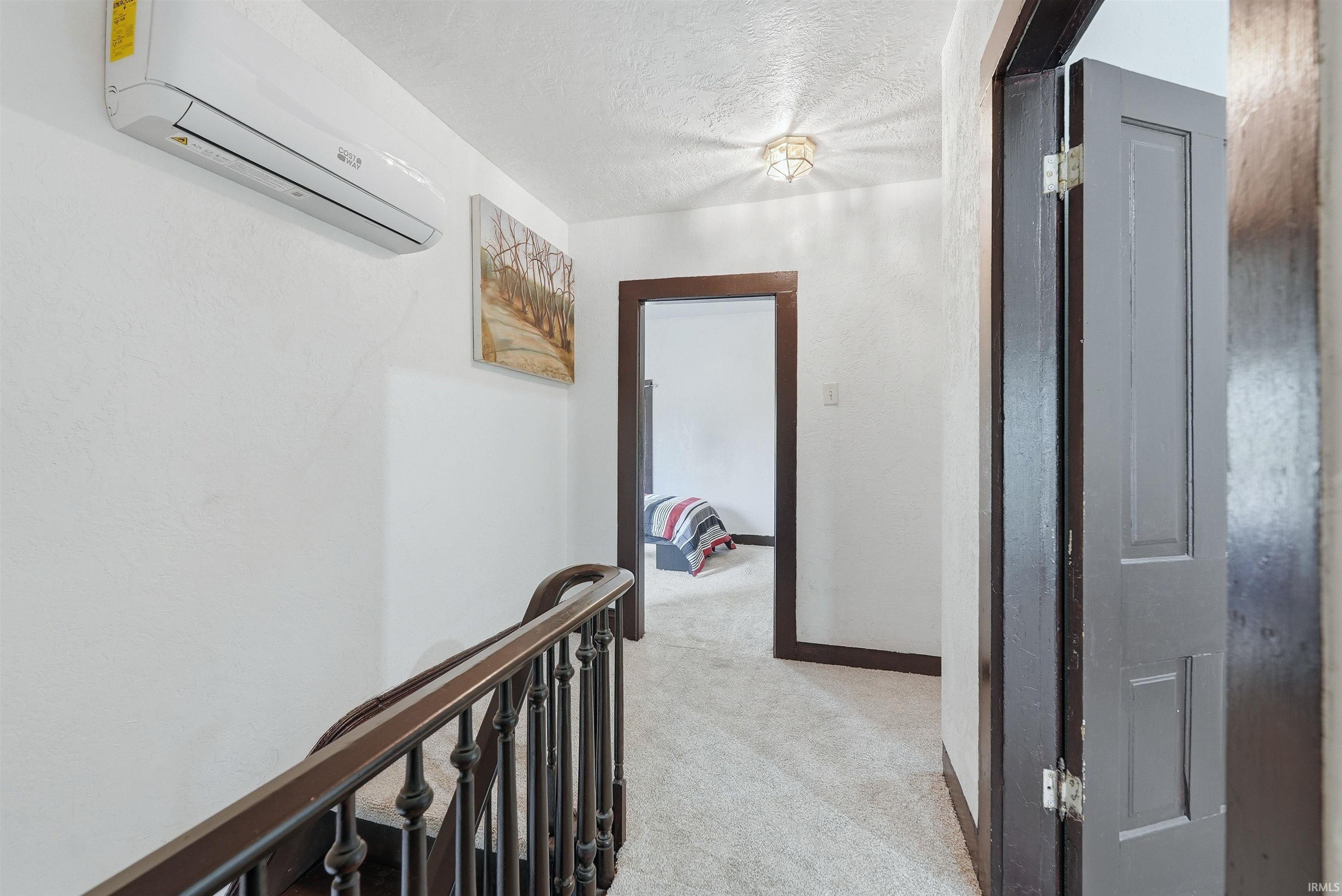 Hallway with light-colored carpet flooring, dark trim around doorways, and a split-system air conditioning unit