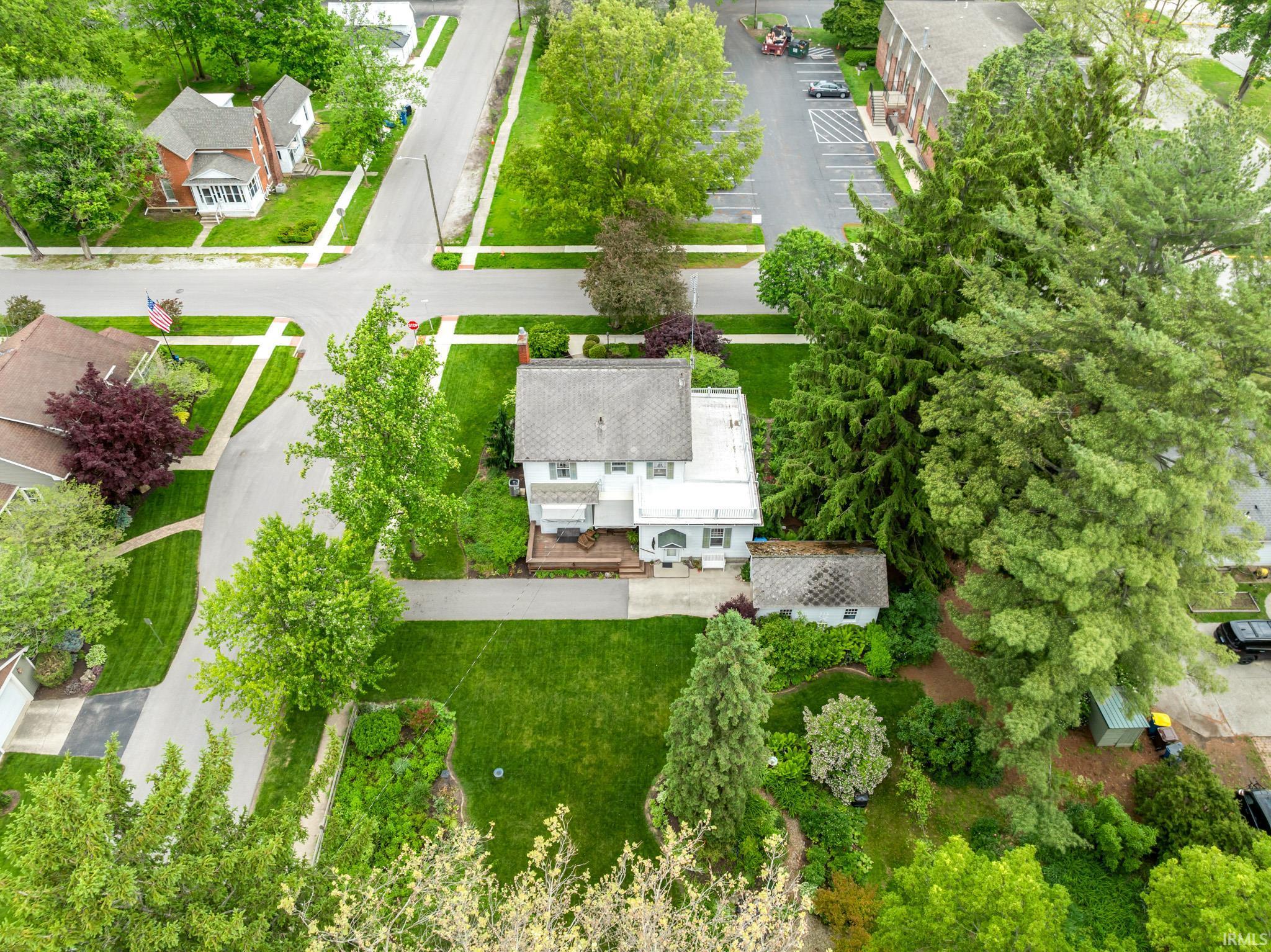 Light-colored residence with a dark roof, featuring a surrounding lawn and established trees