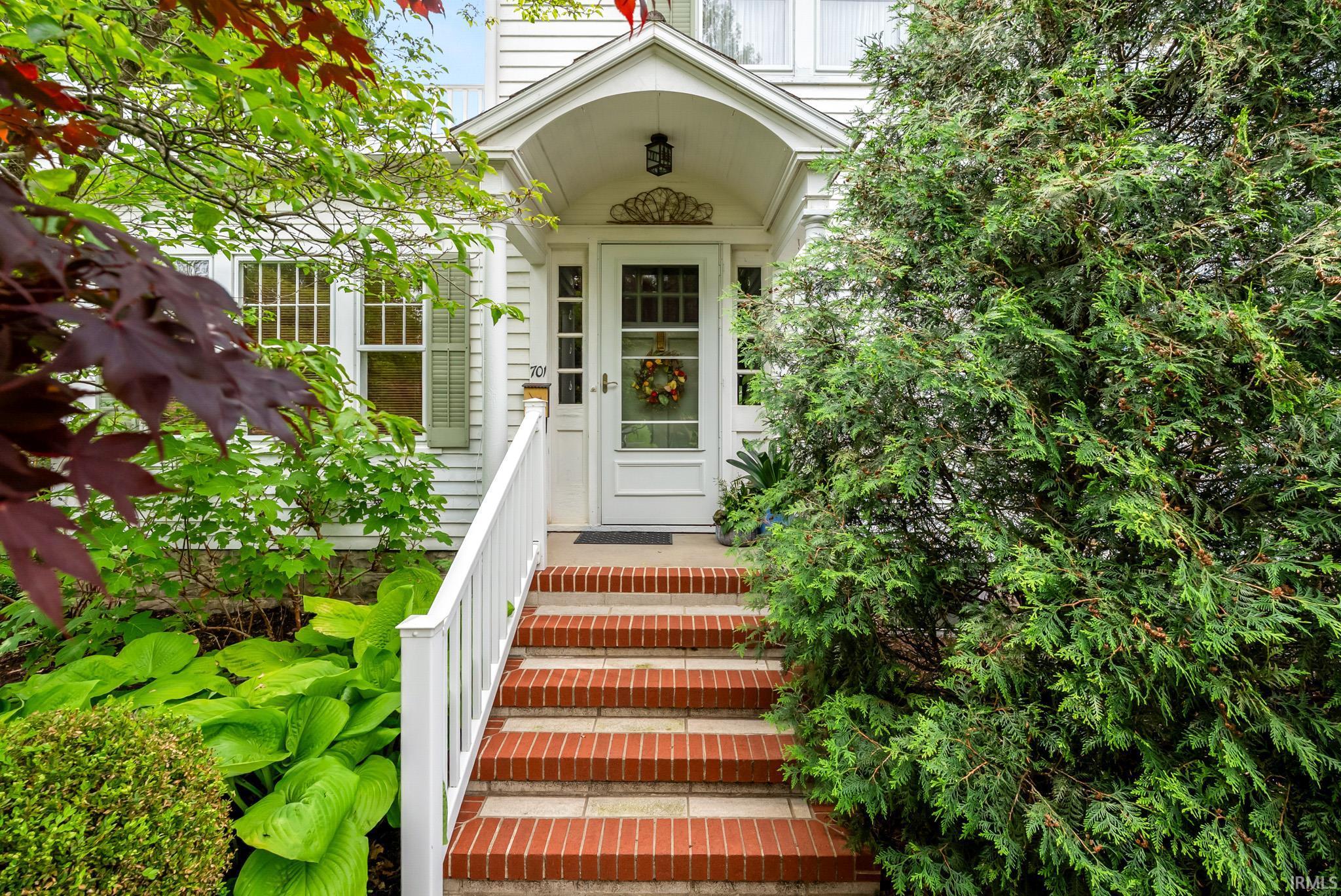 Inviting front entrance featuring a covered porch, brick steps, white railings, and mature landscaping