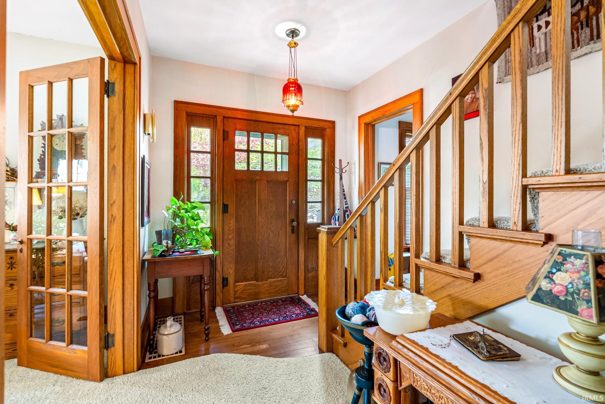 Entryway featuring wood-finish flooring, a solid wood entry door with divided light windows, and a staircase with wood balusters and handrail