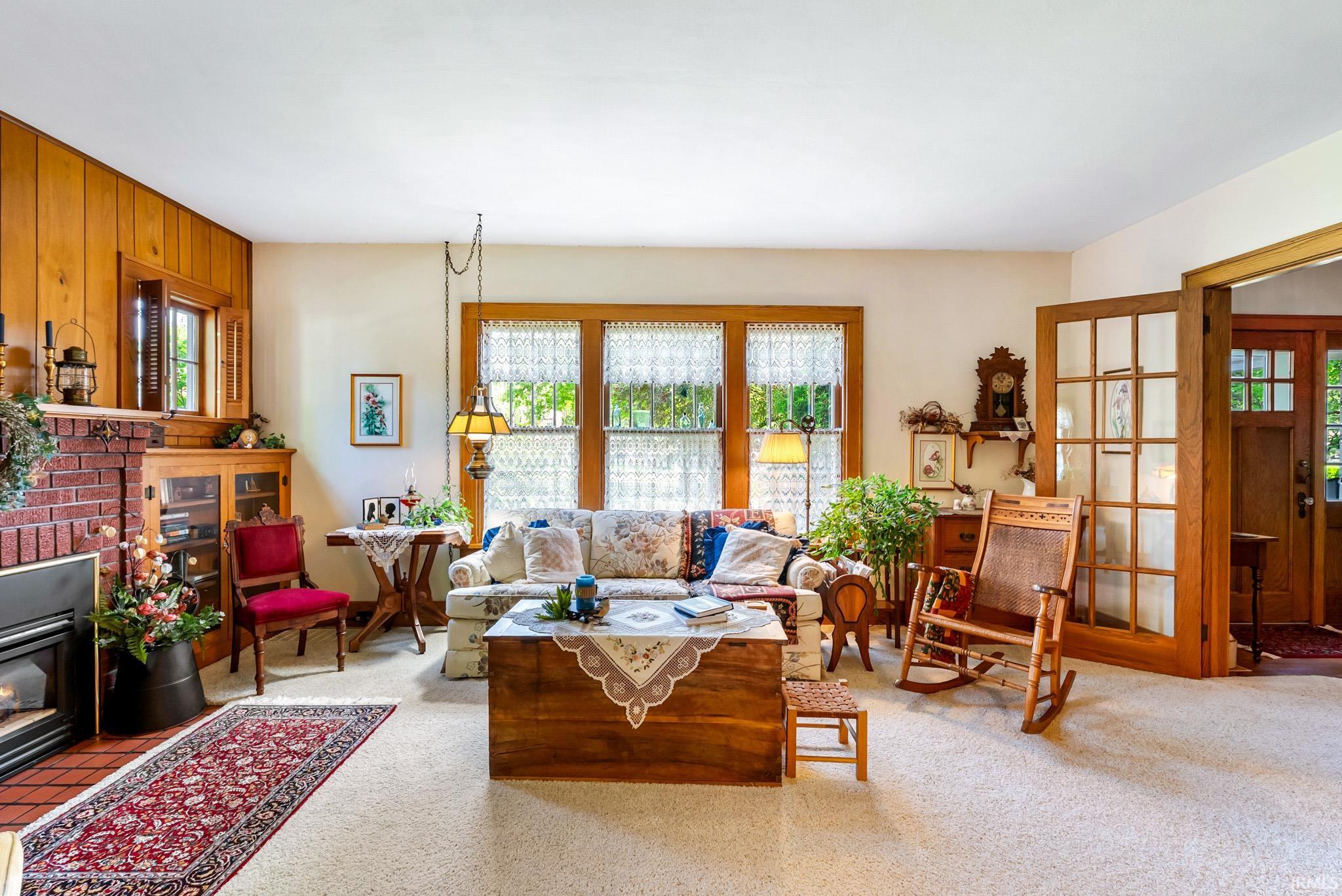 Living room featuring a brick fireplace with a black insert, wood-paneled accent wall, and light-colored carpeting