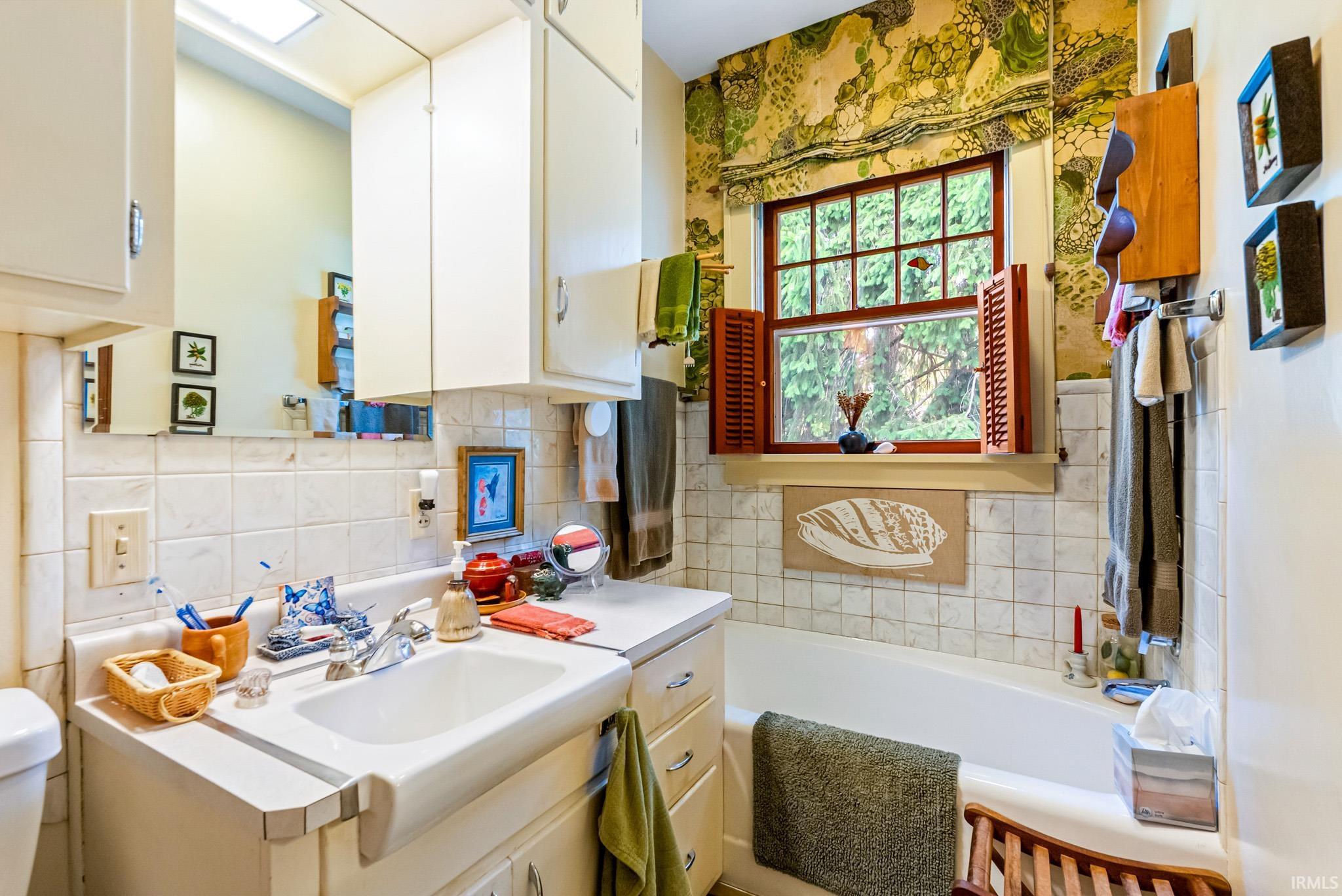 Bathroom featuring a built-in tub, white tile surround, and a window with wooden shutters