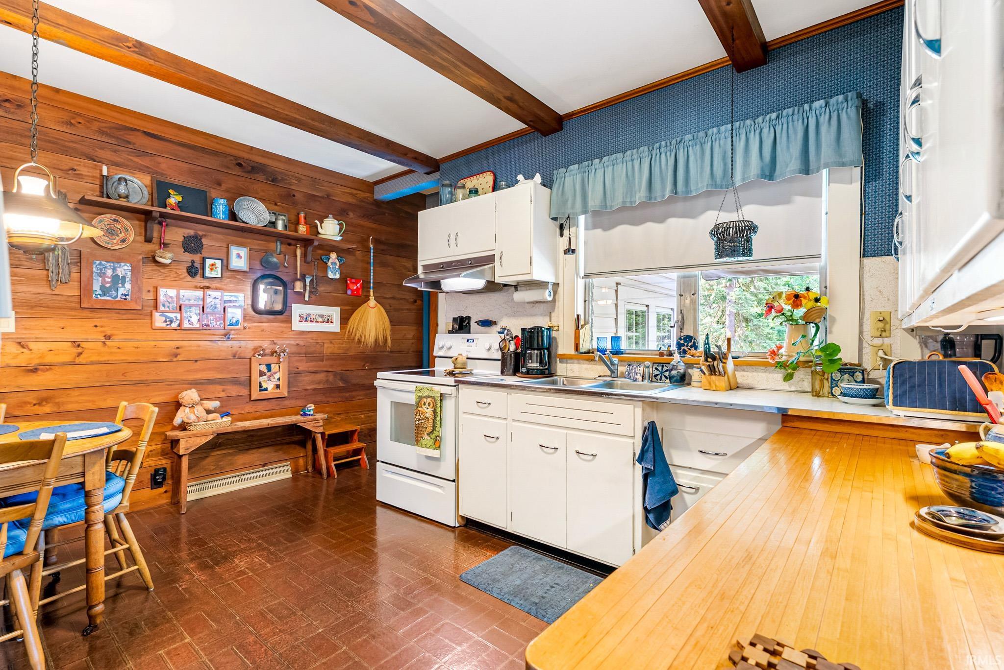Kitchen featuring exposed wood beams, wood-plank wall paneling, brick-patterned flooring, white cabinetry, and a window above the sink