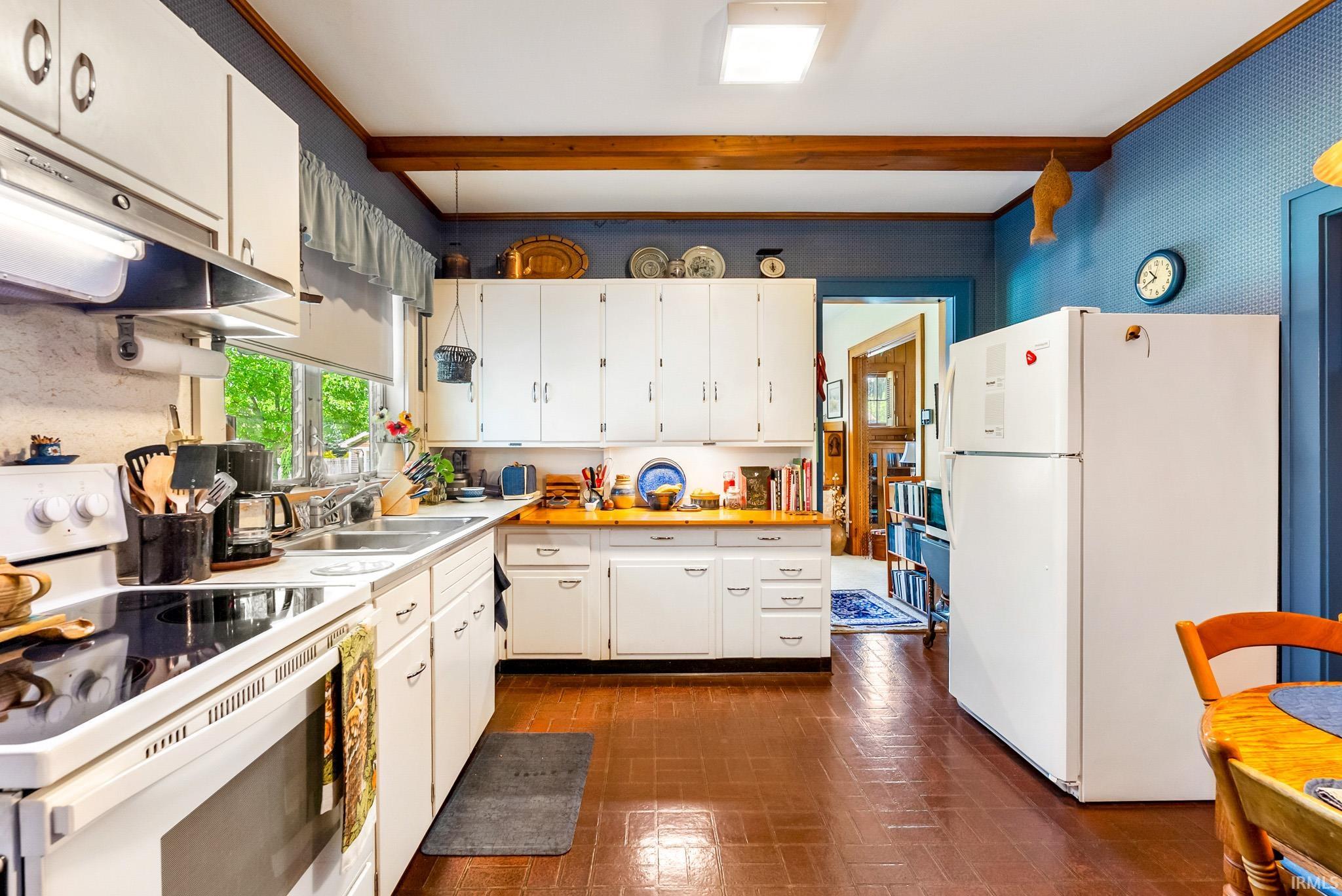 Kitchen featuring extensive white cabinetry, wood-finish countertops, stainless steel sink, built-in range, and wood beam ceiling accents