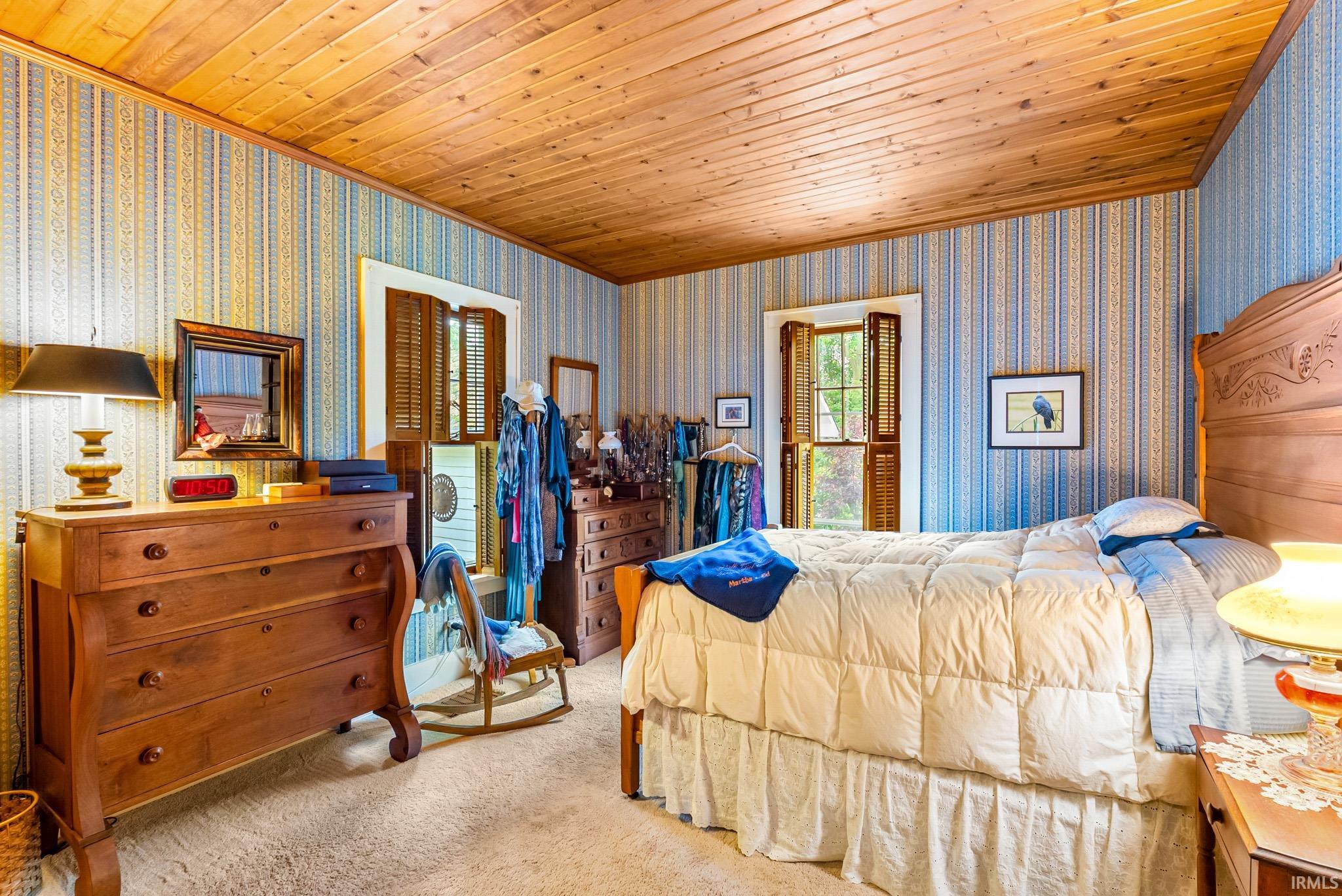 Interior room featuring wood plank ceiling, patterned wallpaper, and soft carpet flooring