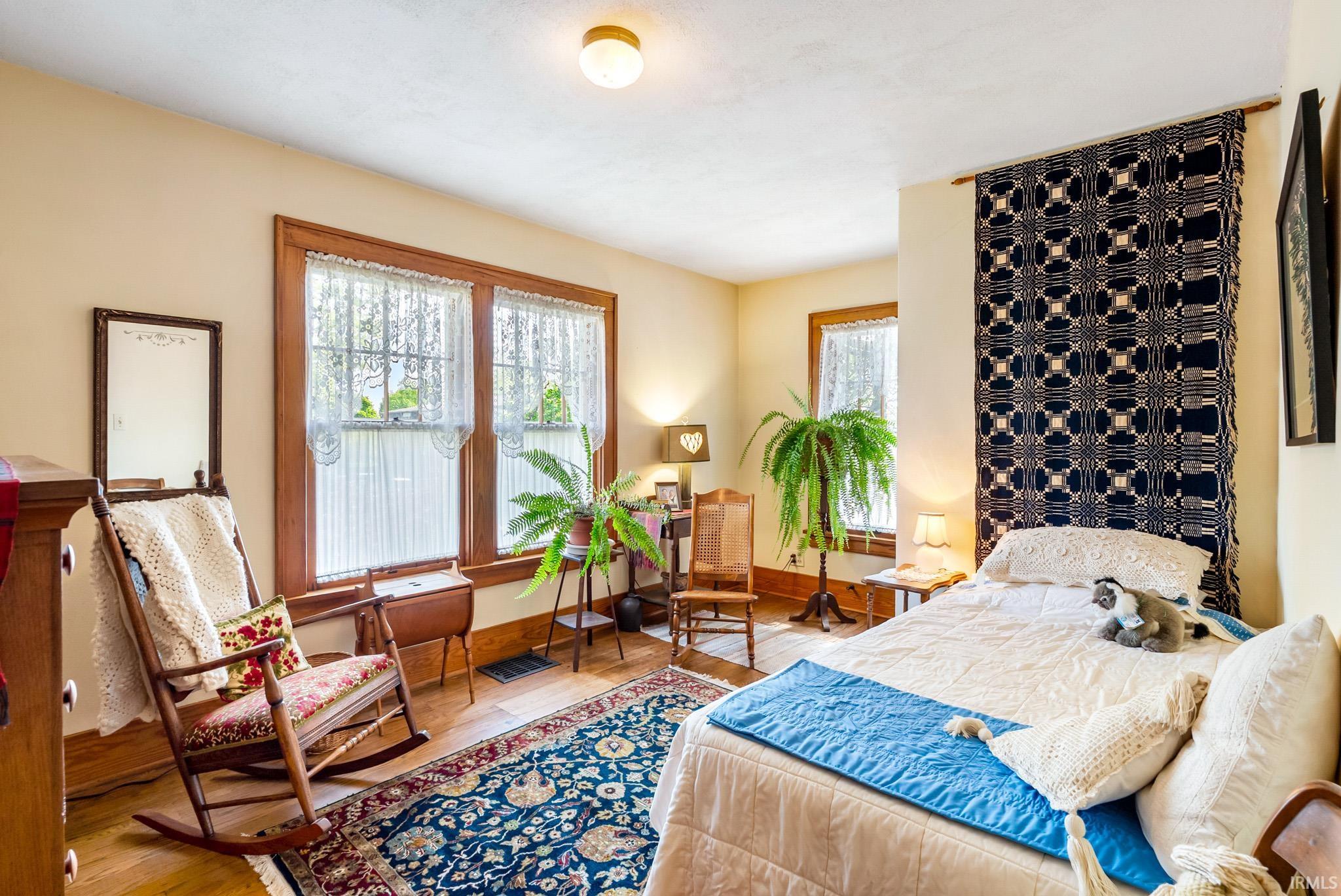 Room with wood-finish flooring, two large windows with lace curtains, and a ceiling-mounted light fixture