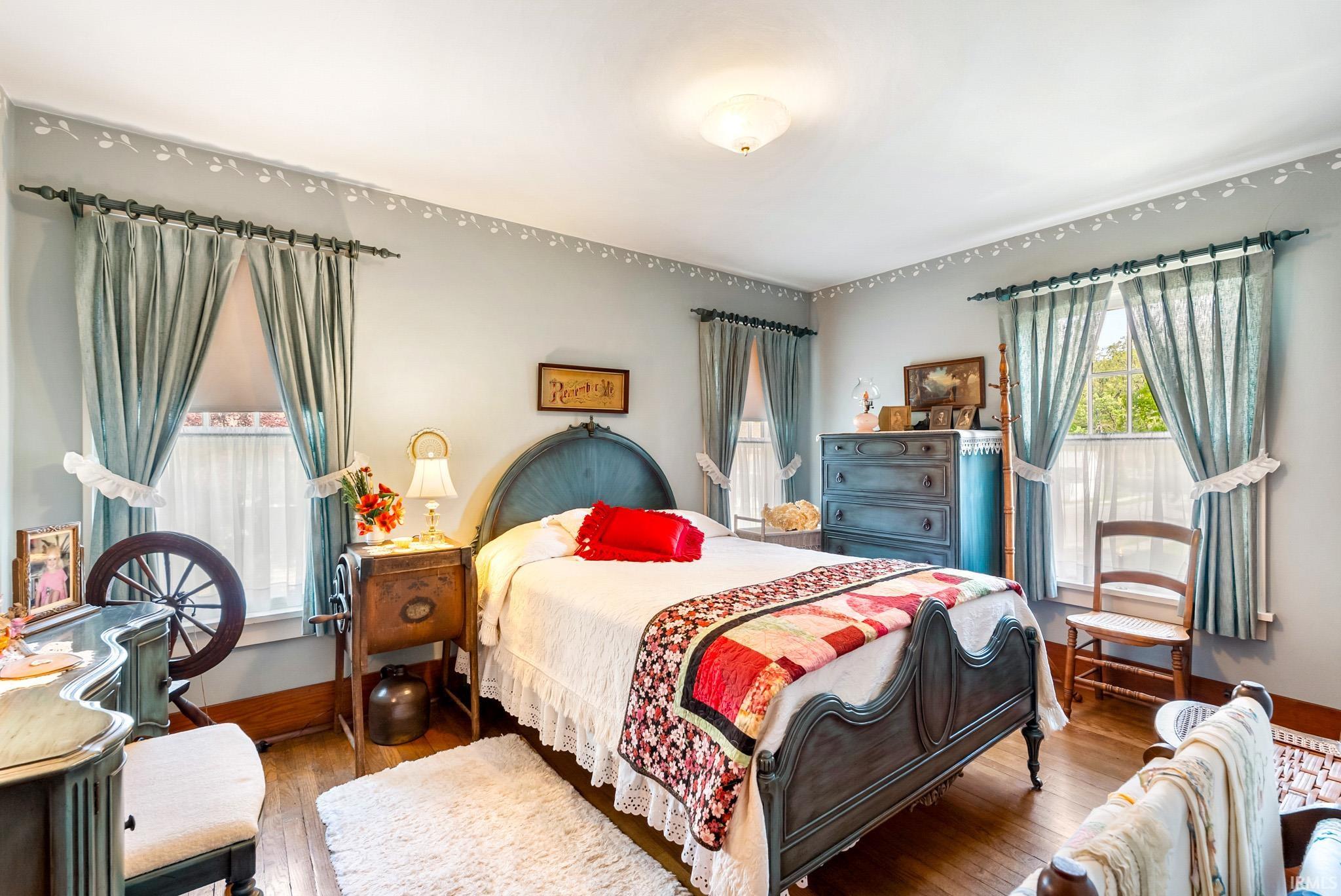 Bedroom featuring two windows with draperies, wood-finish flooring, and a ceiling light fixture