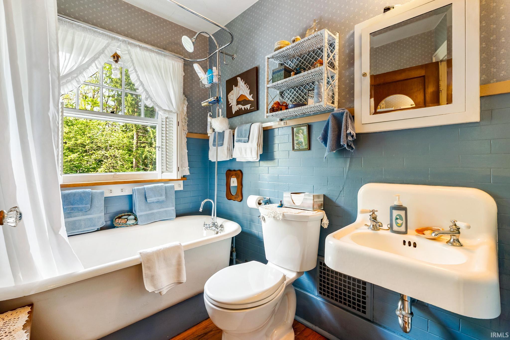 Clawfoot tub with shower attachment and window with exterior landscaping visible