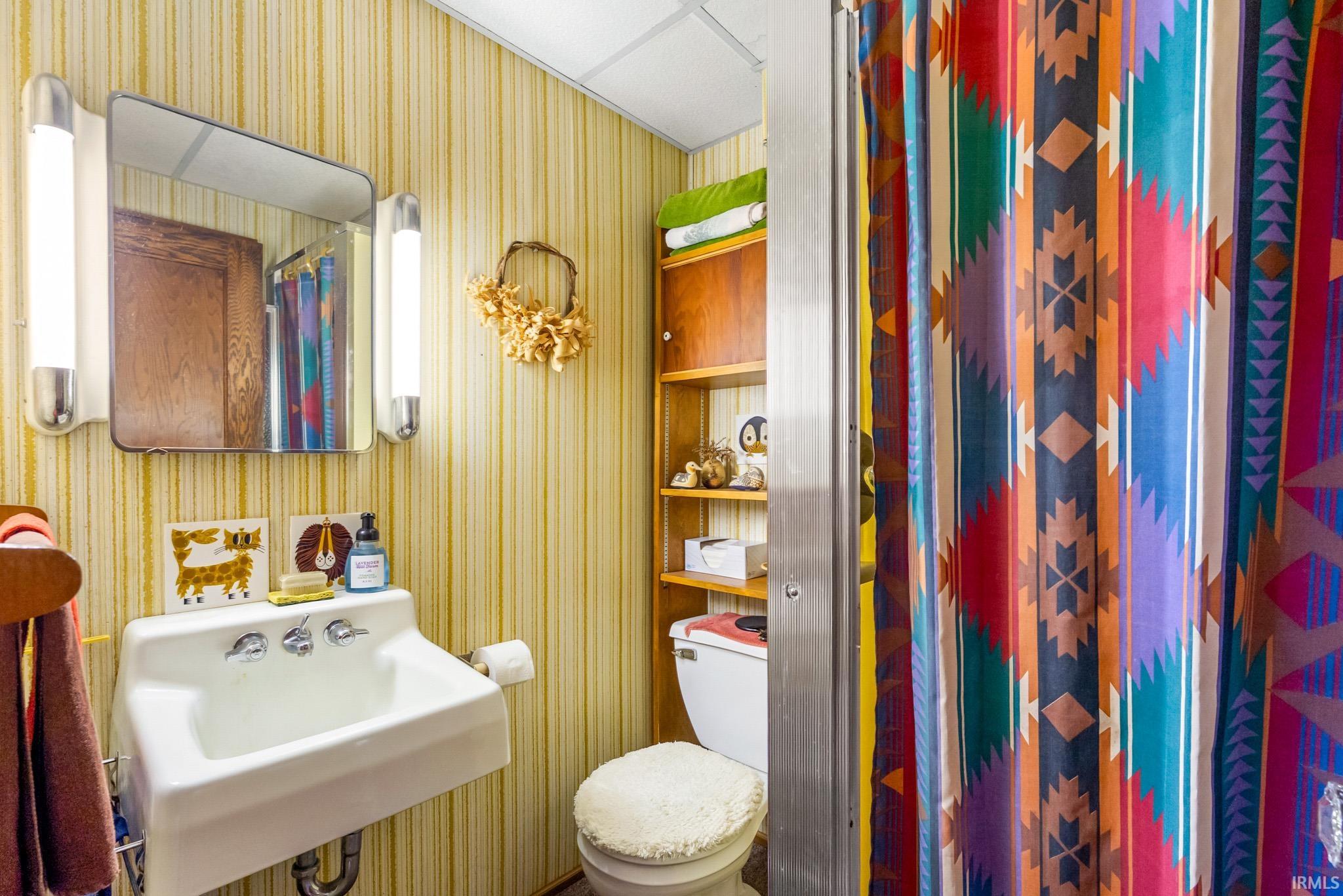 Full bathroom featuring a rectangular wall-mounted sink with chrome fixtures, a mirrored medicine cabinet with flanking tubular light fixtures, and striped wall covering