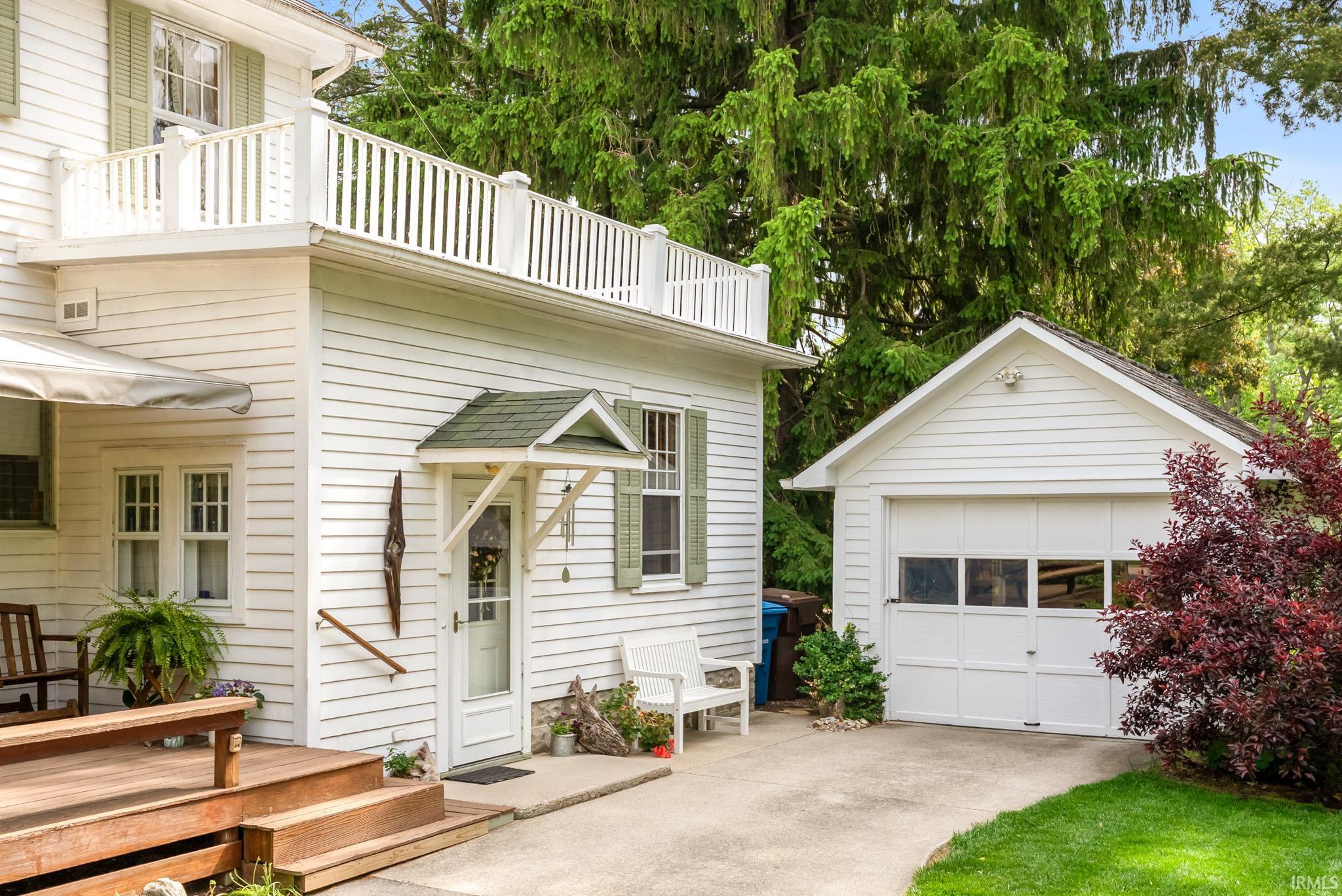 White horizontal siding exterior with a second-story balcony featuring white railing, an attached garage, a side entry with an awning, and a multi-level wood deck