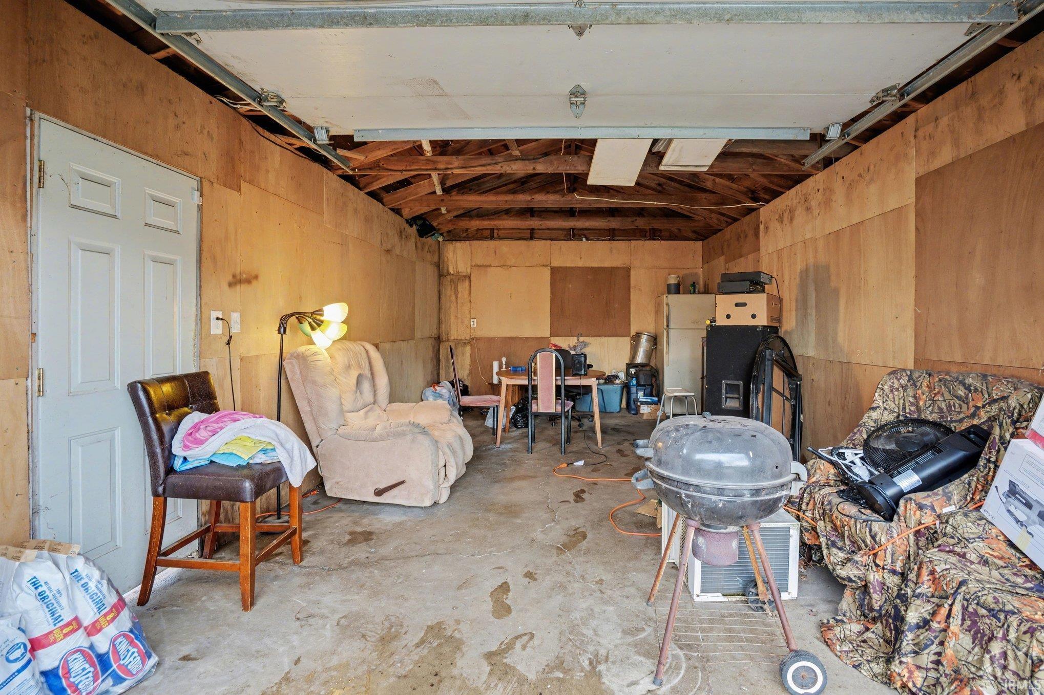 Garage interior with plywood paneling, concrete flooring, and exposed ceiling joists