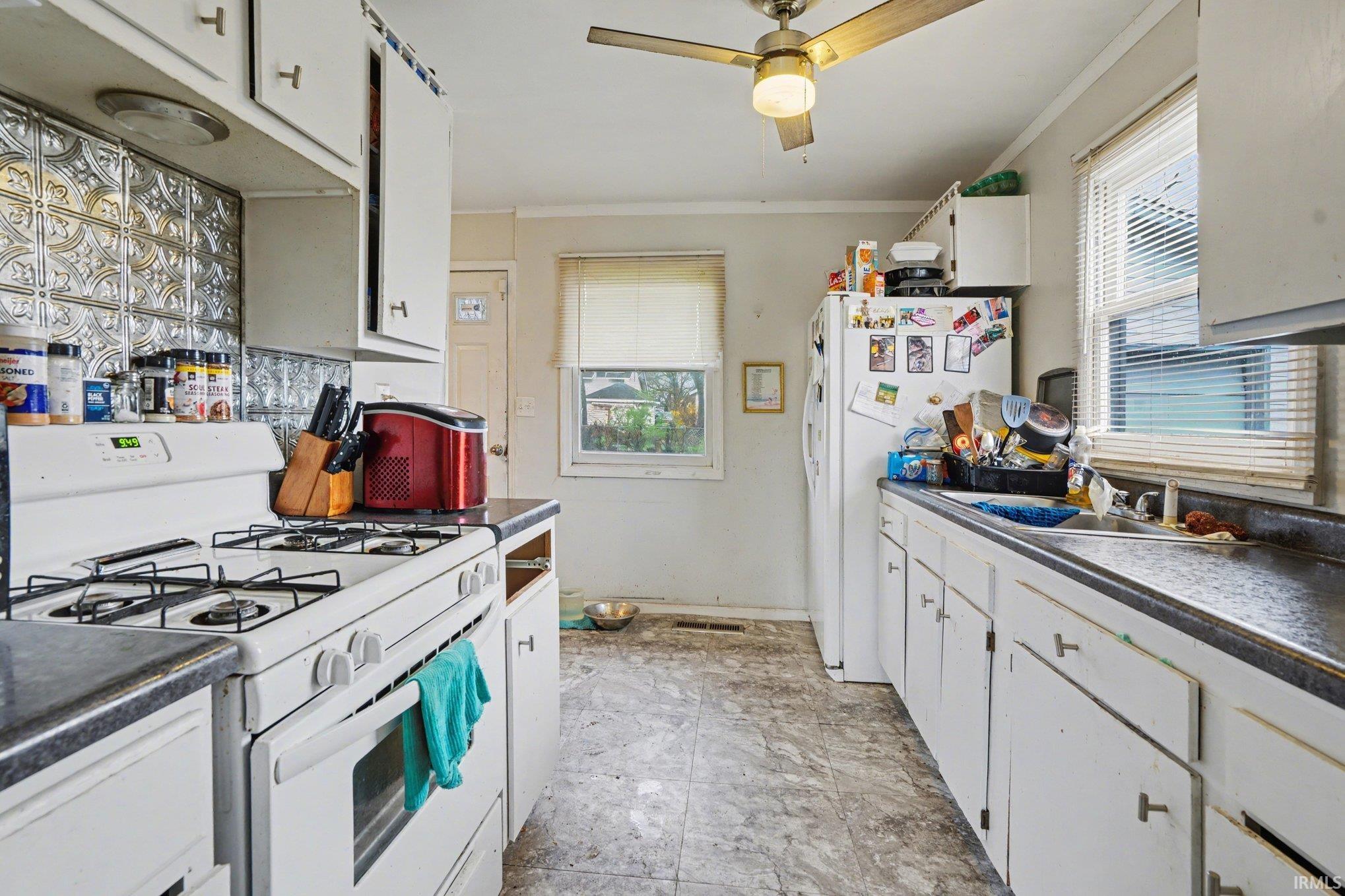 Galley kitchen featuring white cabinetry, a gas range, a dual-basin sink, and a ceiling fan