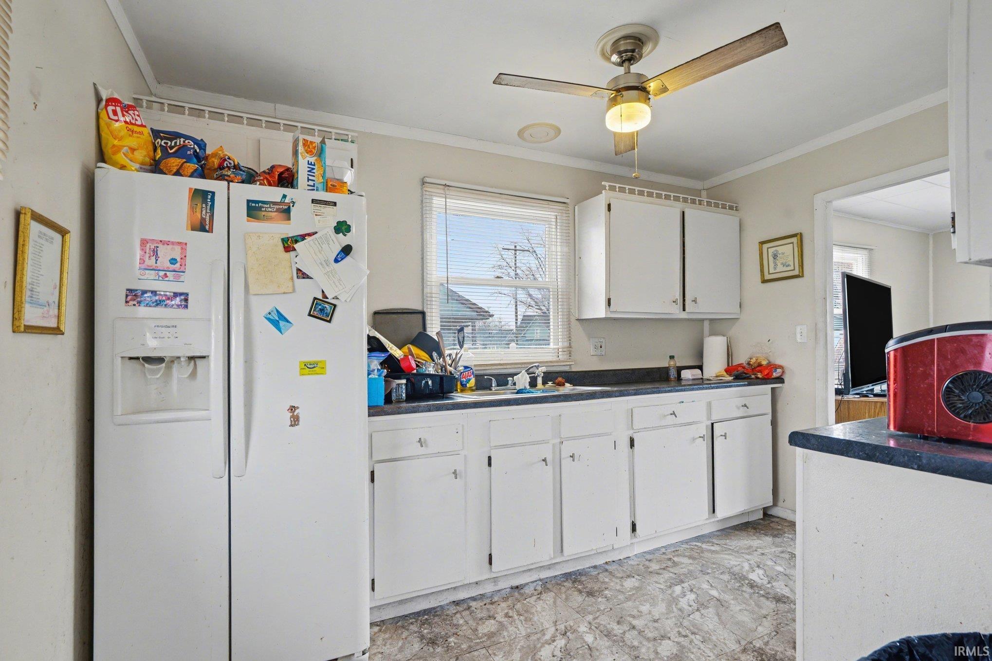 Kitchen area featuring a window, white cabinetry, dark countertops, and a ceiling fan