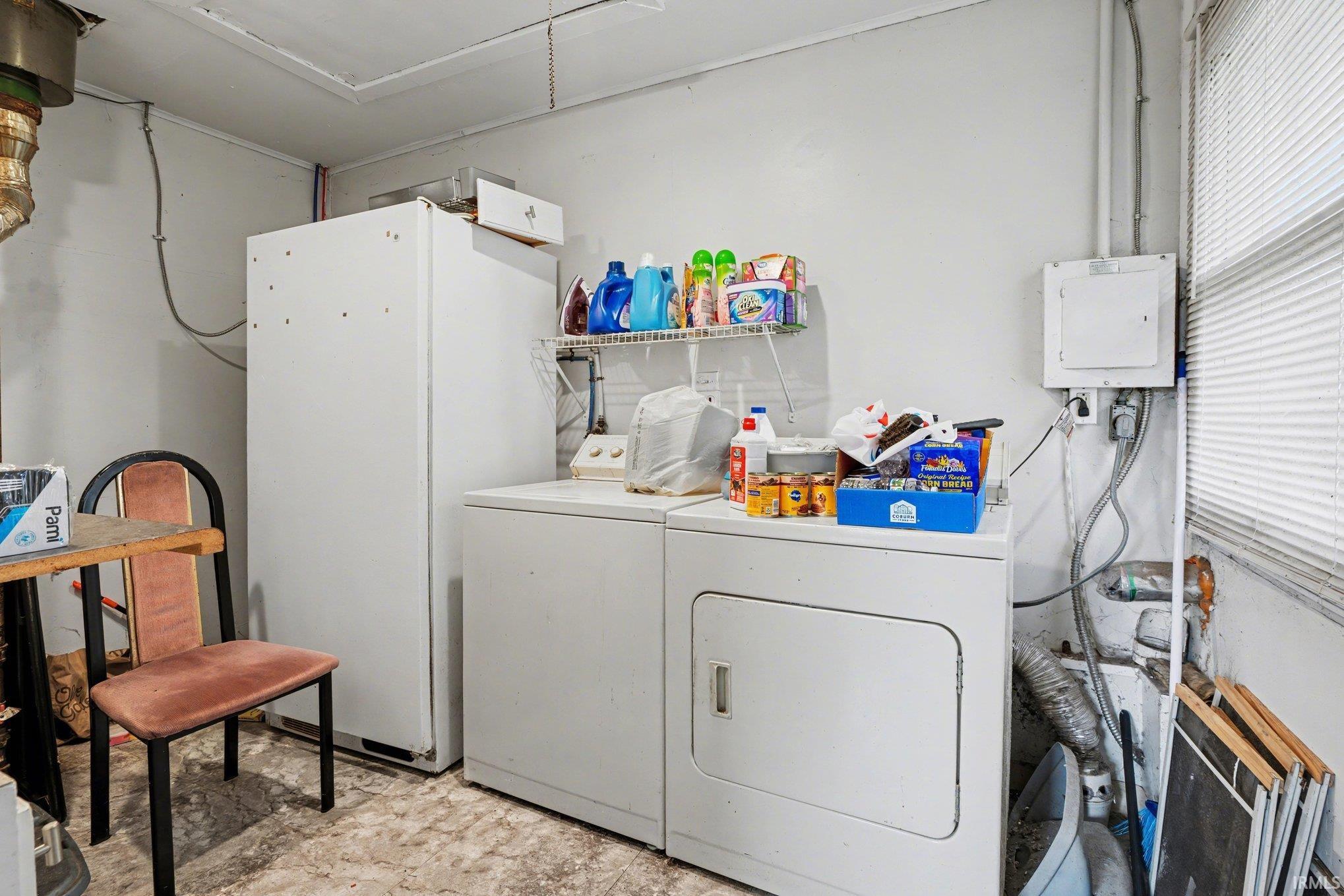 Dedicated laundry area featuring a white washing machine and dryer, a white upright freezer, and a wall-mounted wire shelf