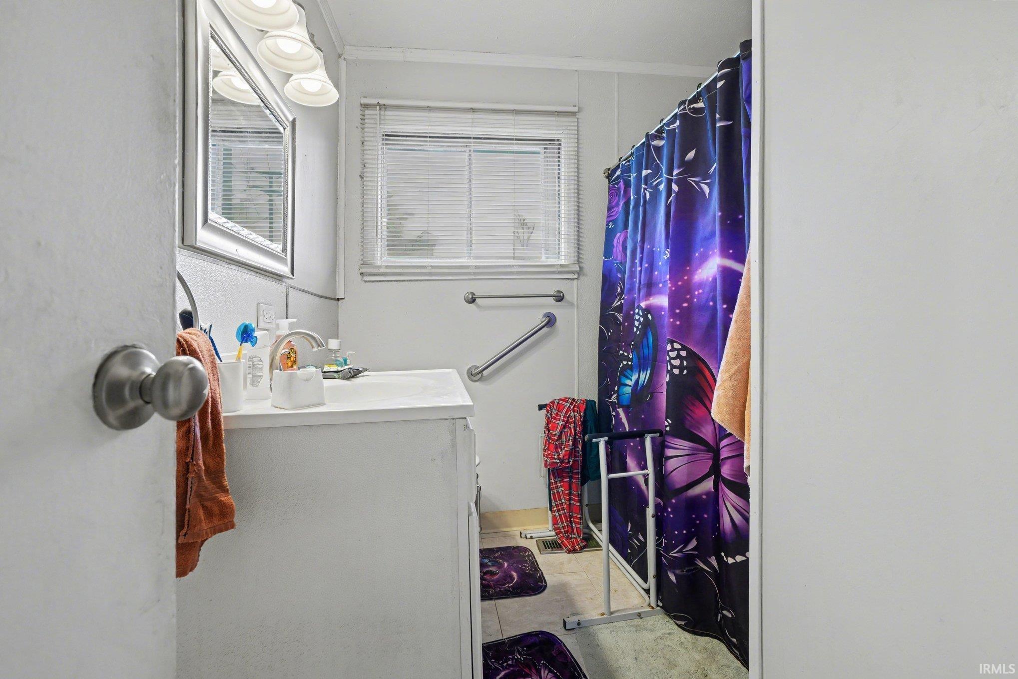 Bathroom featuring a single vanity with an integrated sink, a mirrored medicine cabinet, a window with horizontal blinds, and wall-mounted grab bars