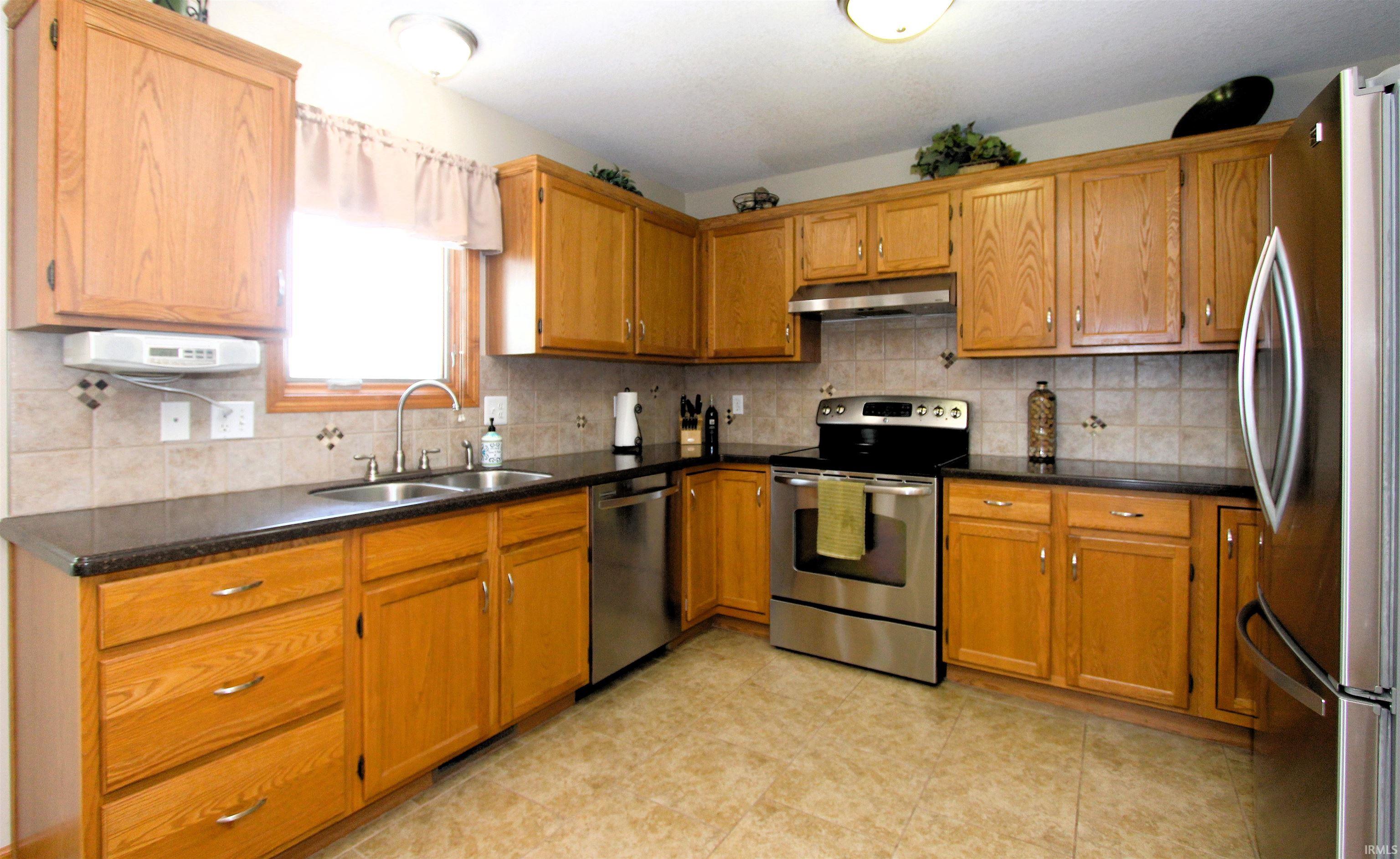 Kitchen featuring light wood cabinetry, dark countertops, a stainless steel refrigerator, and a stainless steel range with overhead ventilation