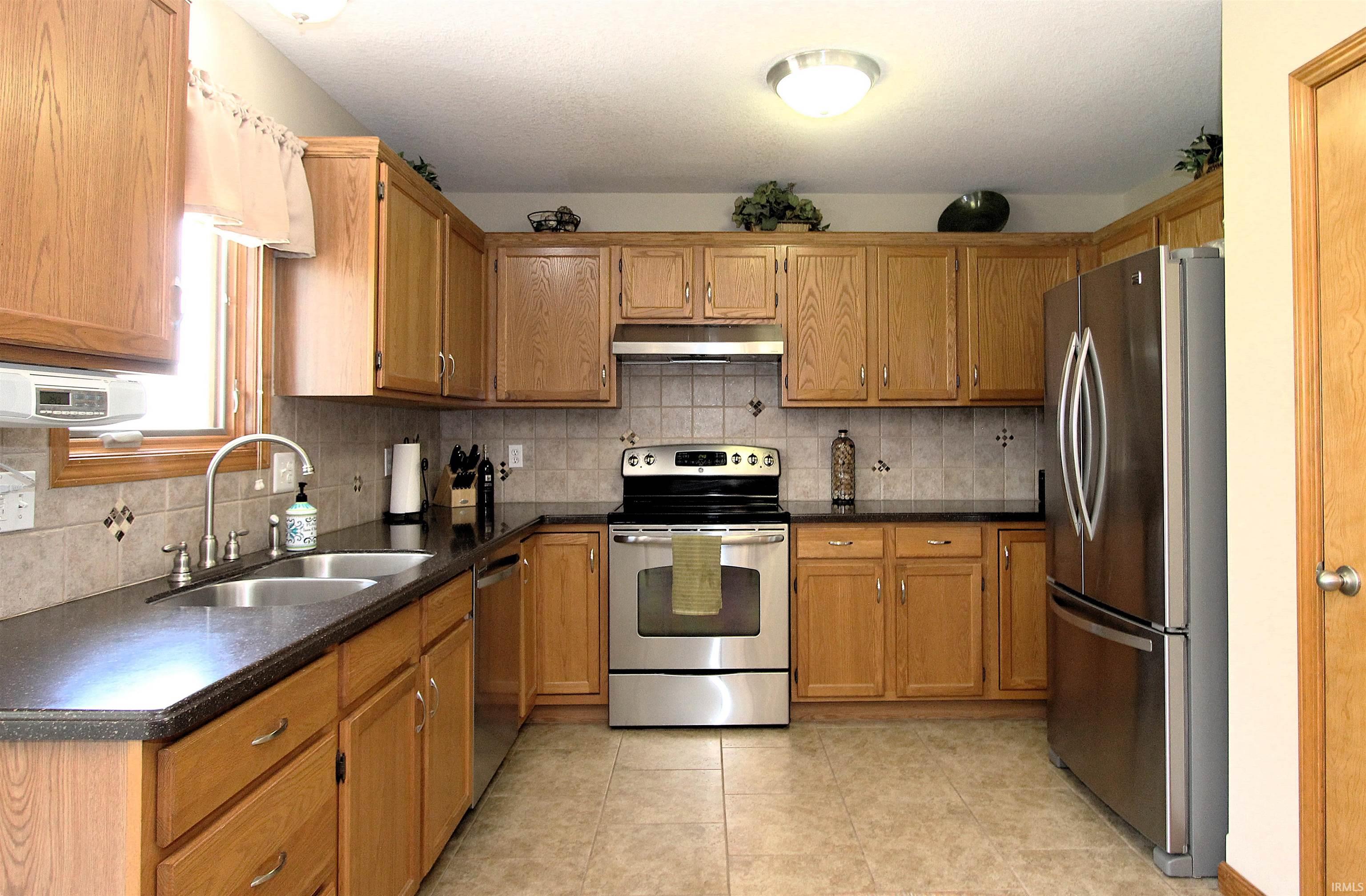 Kitchen featuring wood cabinetry, dark countertops, a tile backsplash, stainless steel appliances, and tile flooring