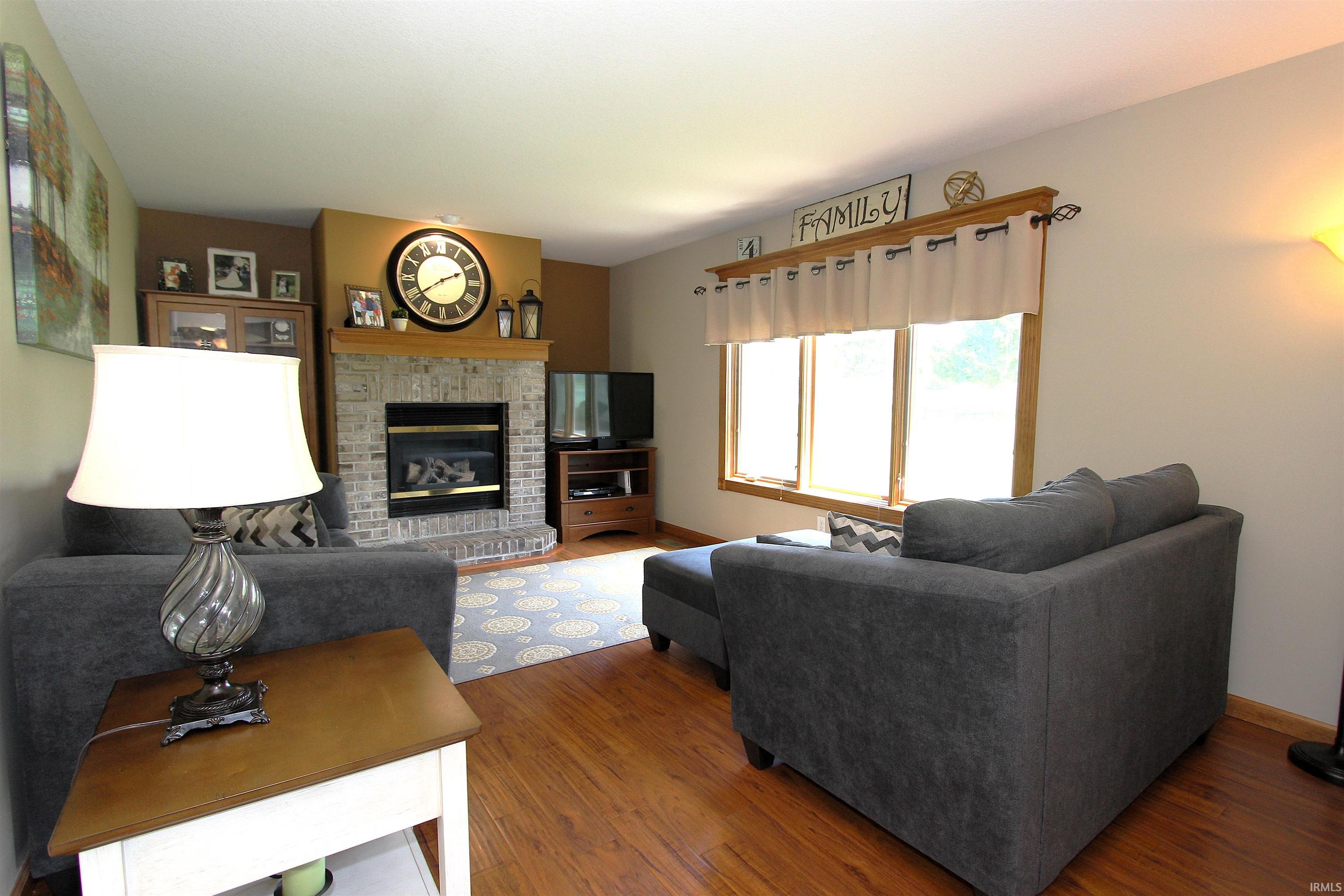 Living area featuring wood-finish flooring, a brick fireplace with a wood mantle, and a large multi-pane window