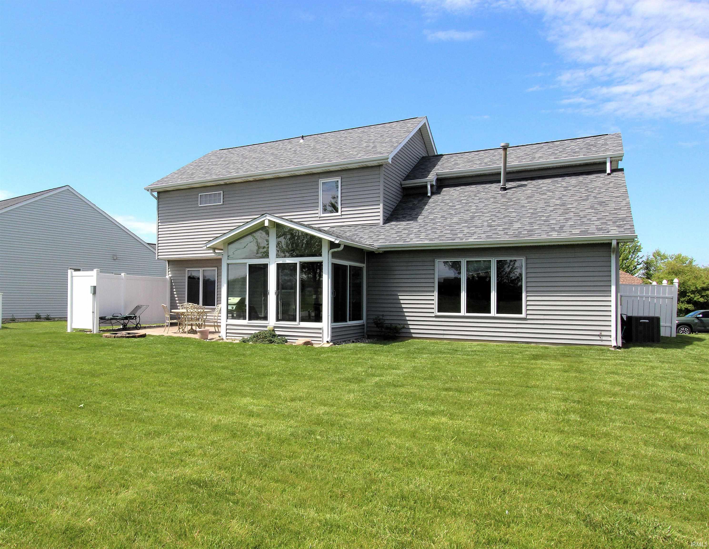 Rear exterior featuring gray vinyl siding, a sunroom with expansive windows, a concrete patio, a white privacy fence, and a large grassy yard